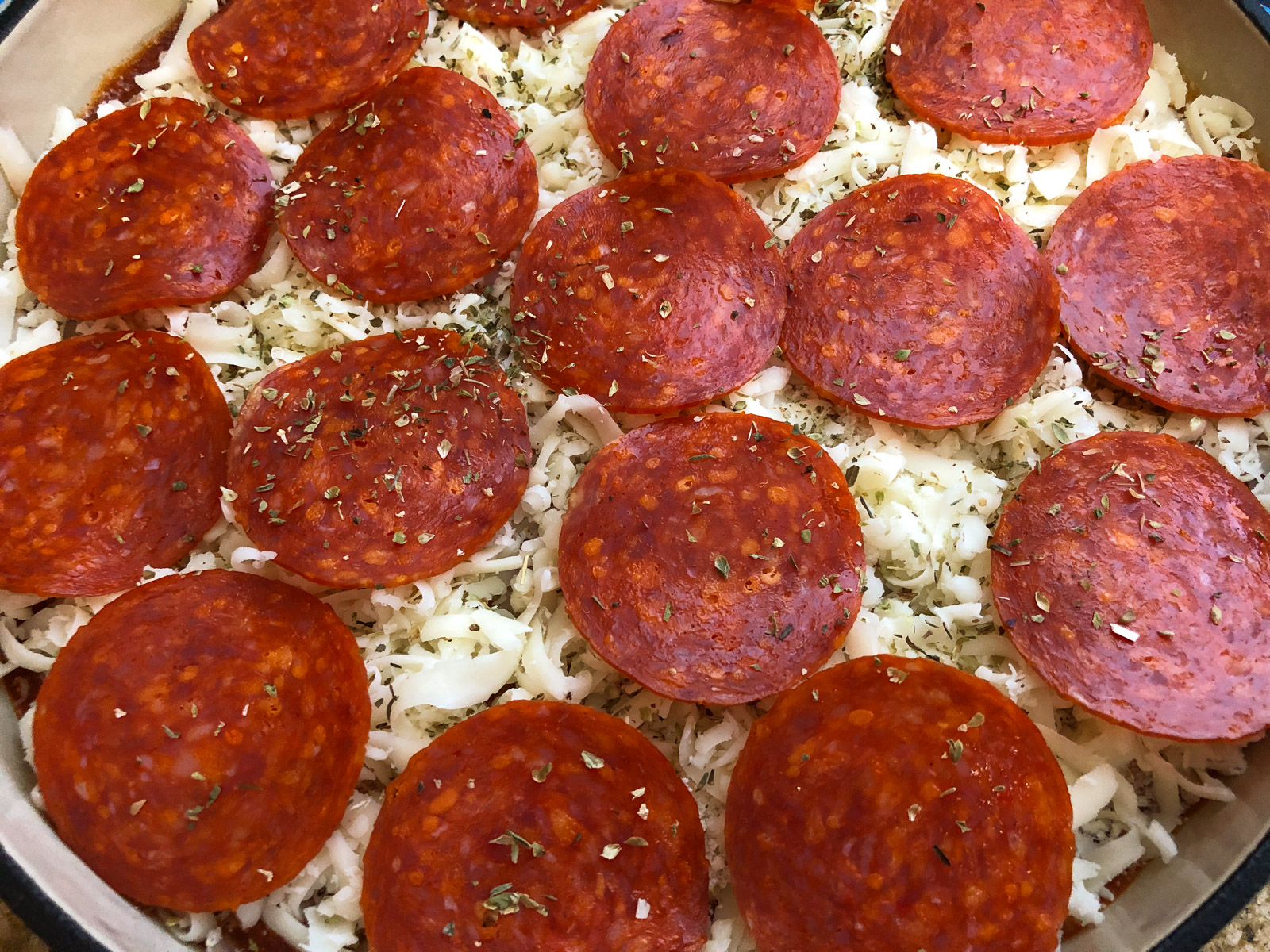 Pepperoni slices arranged on top of shredded mozzarella cheese before baking.