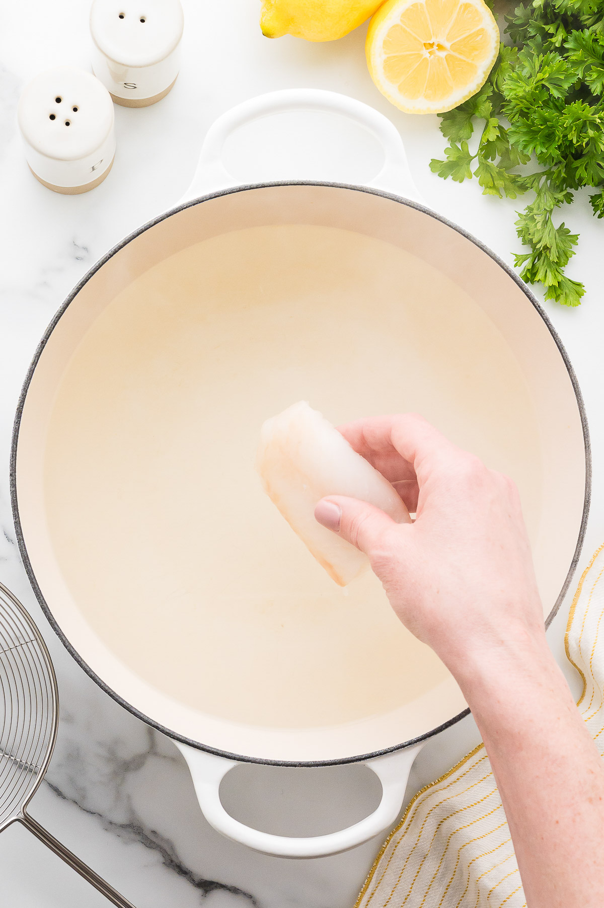 Hand lowering a piece of cod into Dutch oven with sugar water poaching liquid