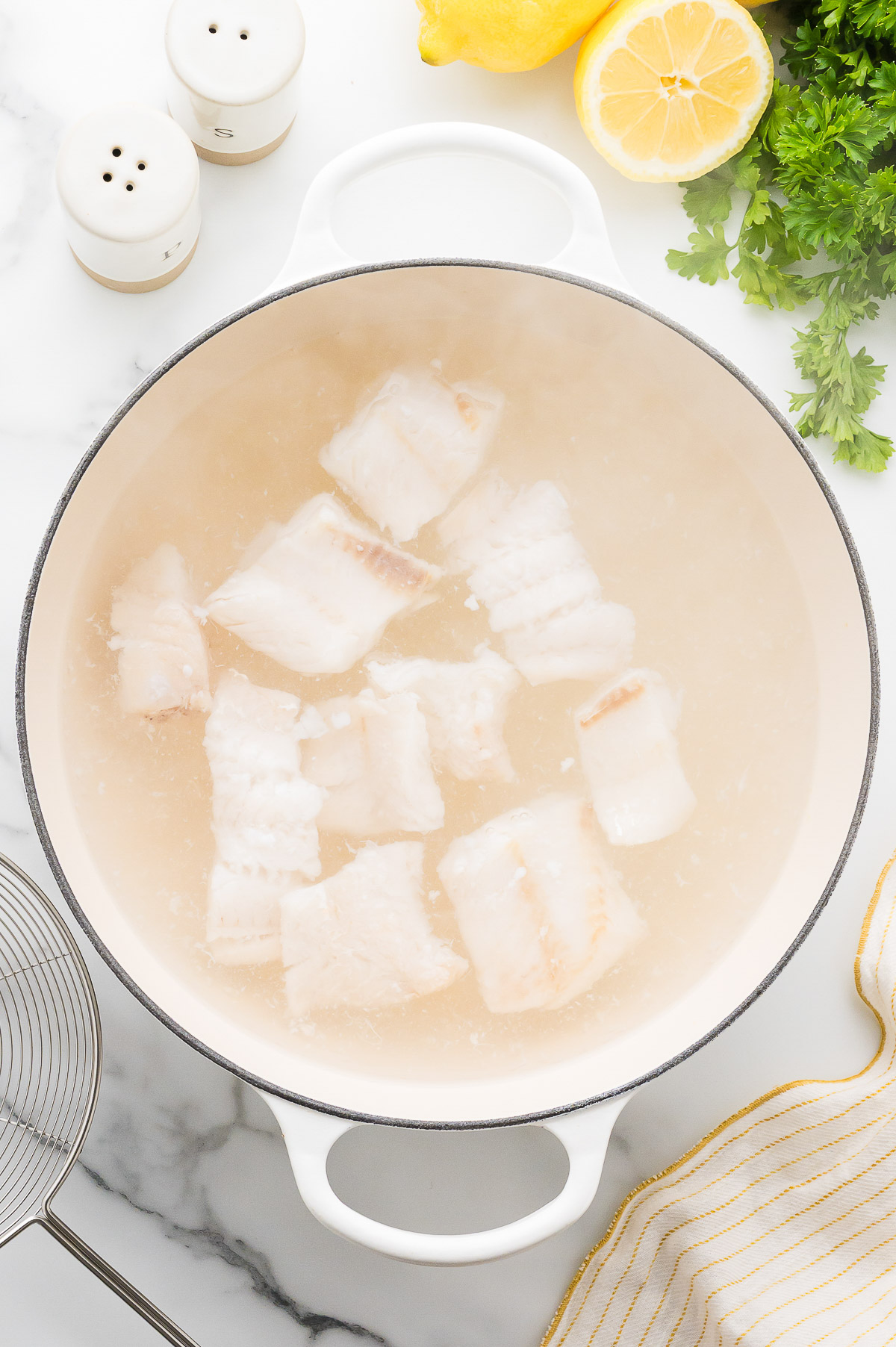 Cod chunks poaching in sugar water in a Dutch oven