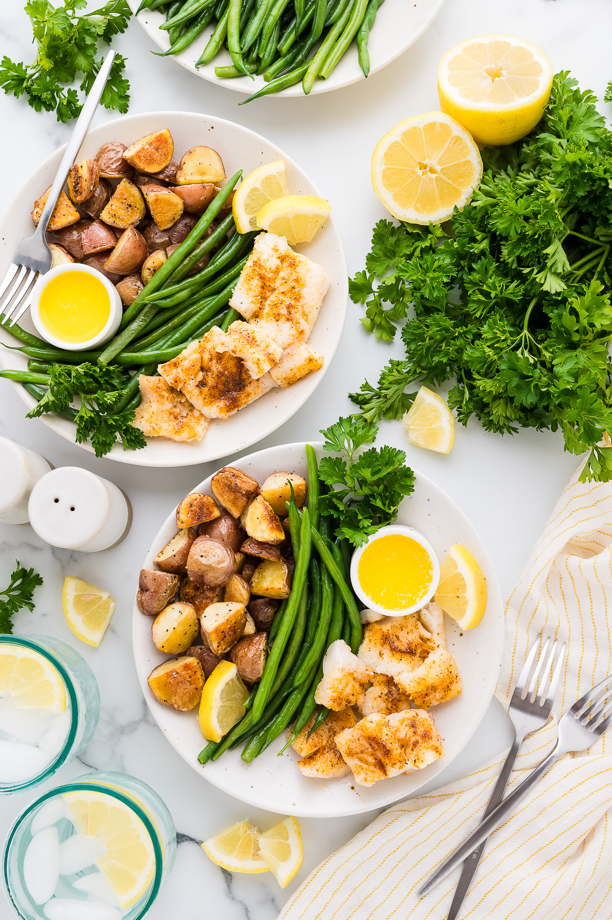 Two plates of poor mans lobster cod with roasted potatoes green beans butter and lemon wedges