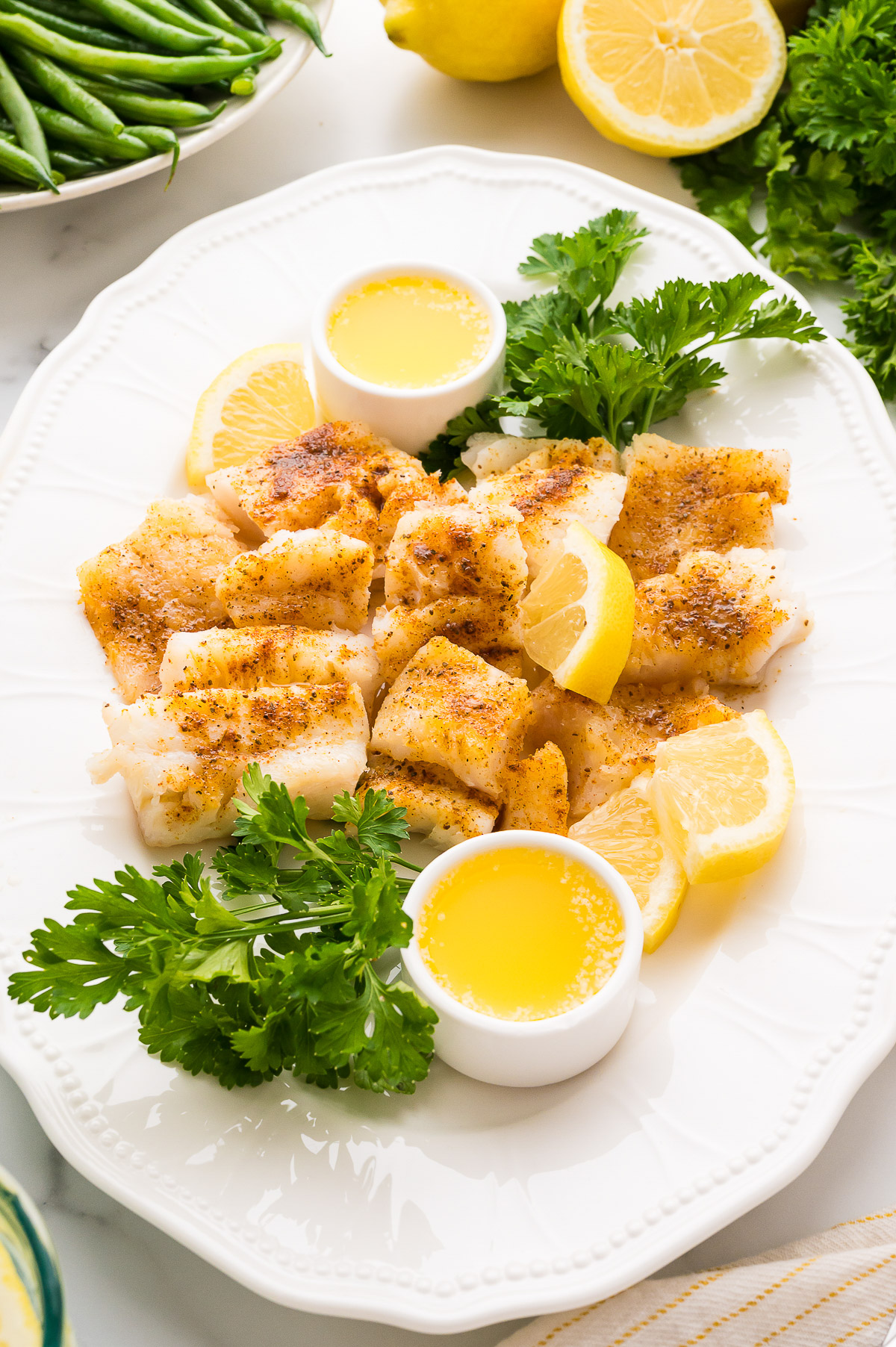 Poor mans lobster cod arranged on oval platter with butter cups and lemon