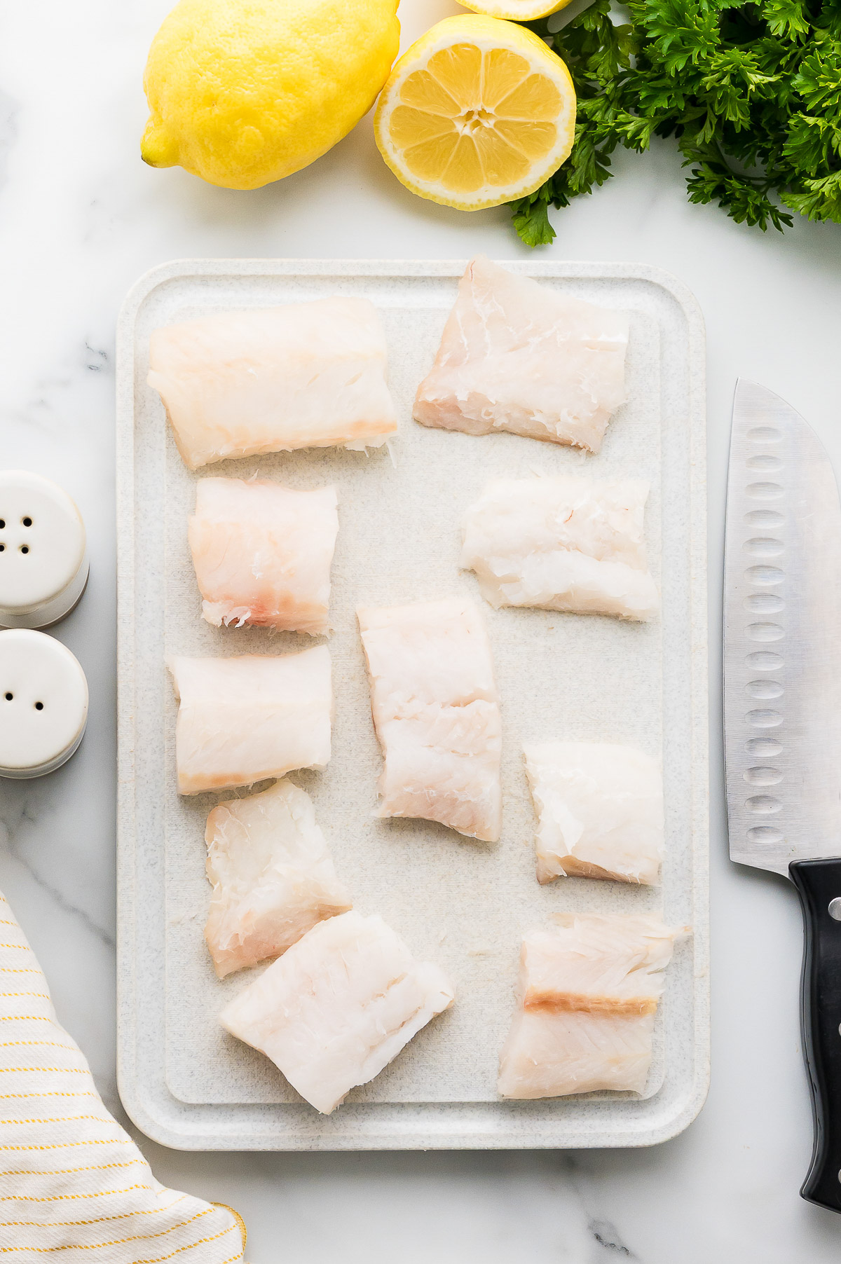 Raw cod fillets on cutting board with lemons and knife