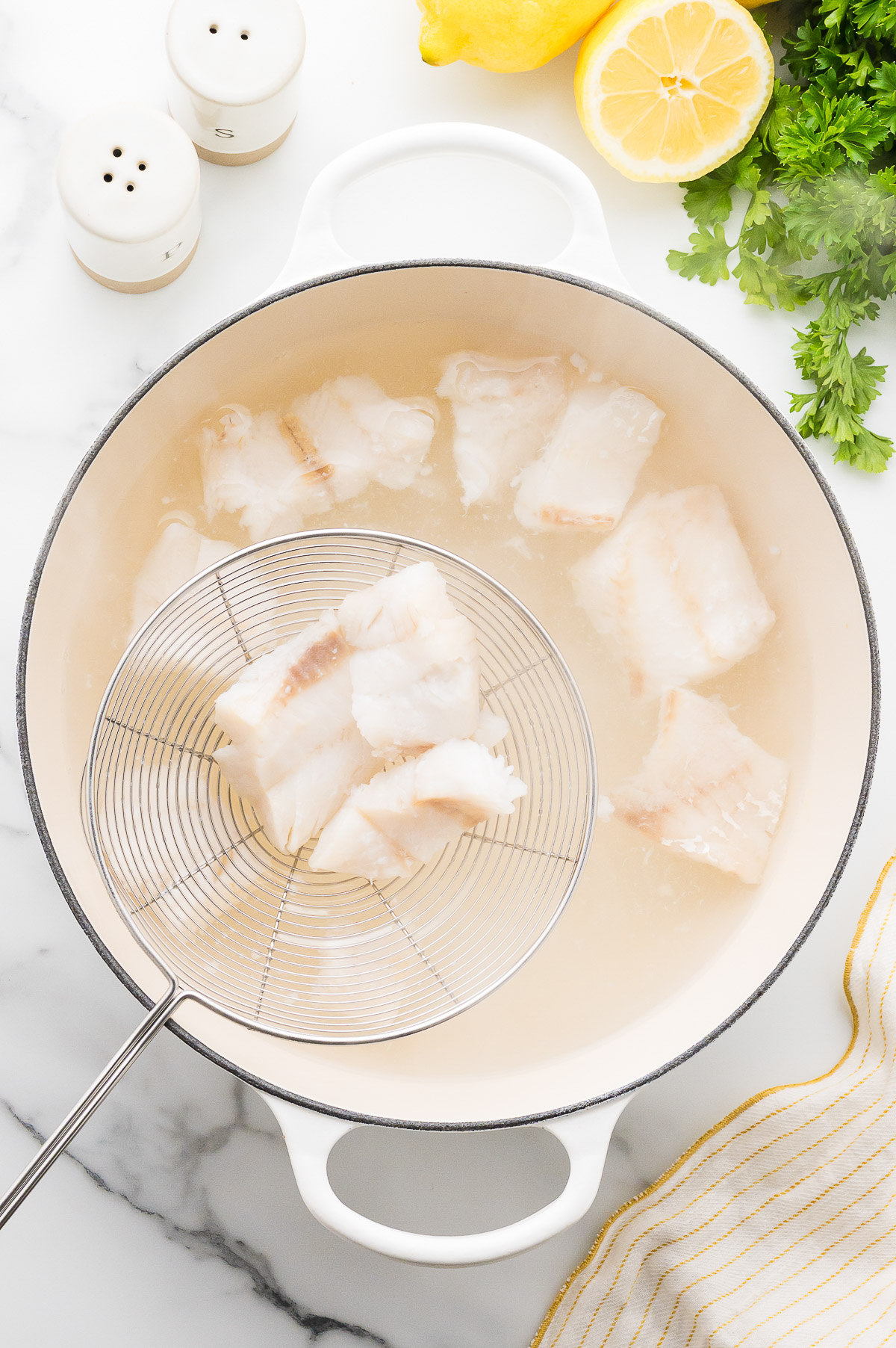 Scooping cooked poor mans lobster cod out of Dutch oven with wire strainer