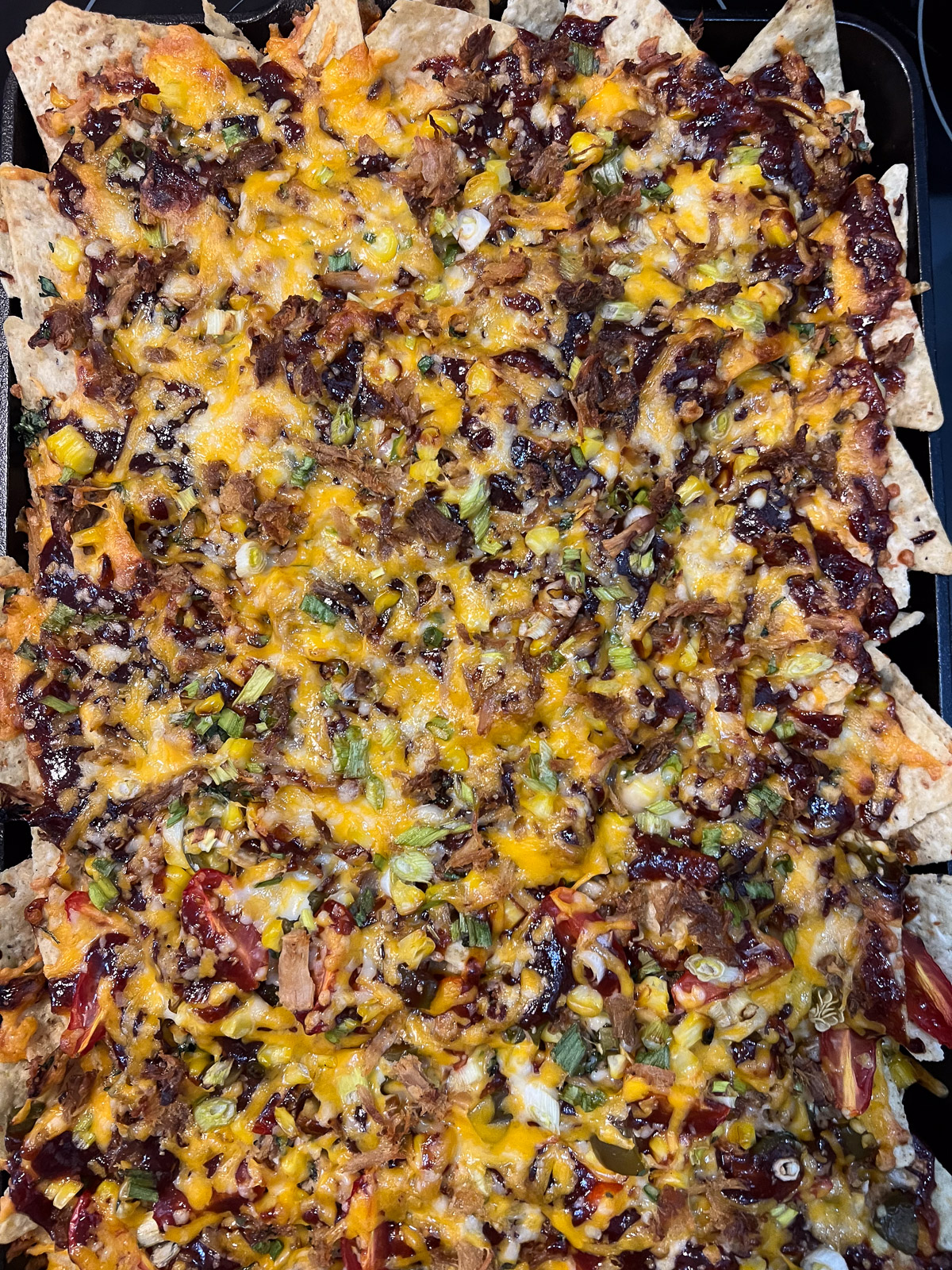 Pulled pork nachos fresh from the oven with golden melted cheese on a cast iron baking sheet