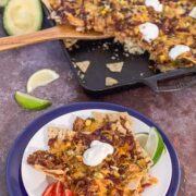 A serving of pulled pork nachos on a blue plate with lime wedges and grape tomatoes