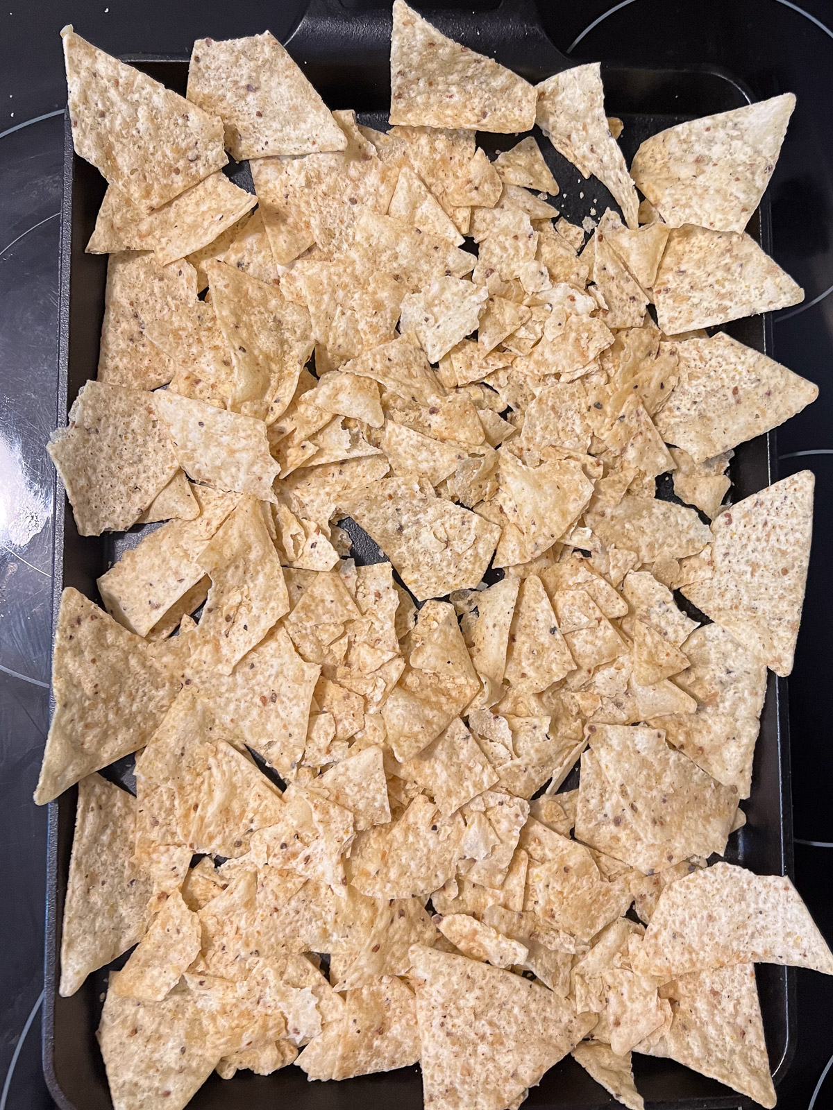 First layer of tortilla chips spread across a cast iron baking sheet