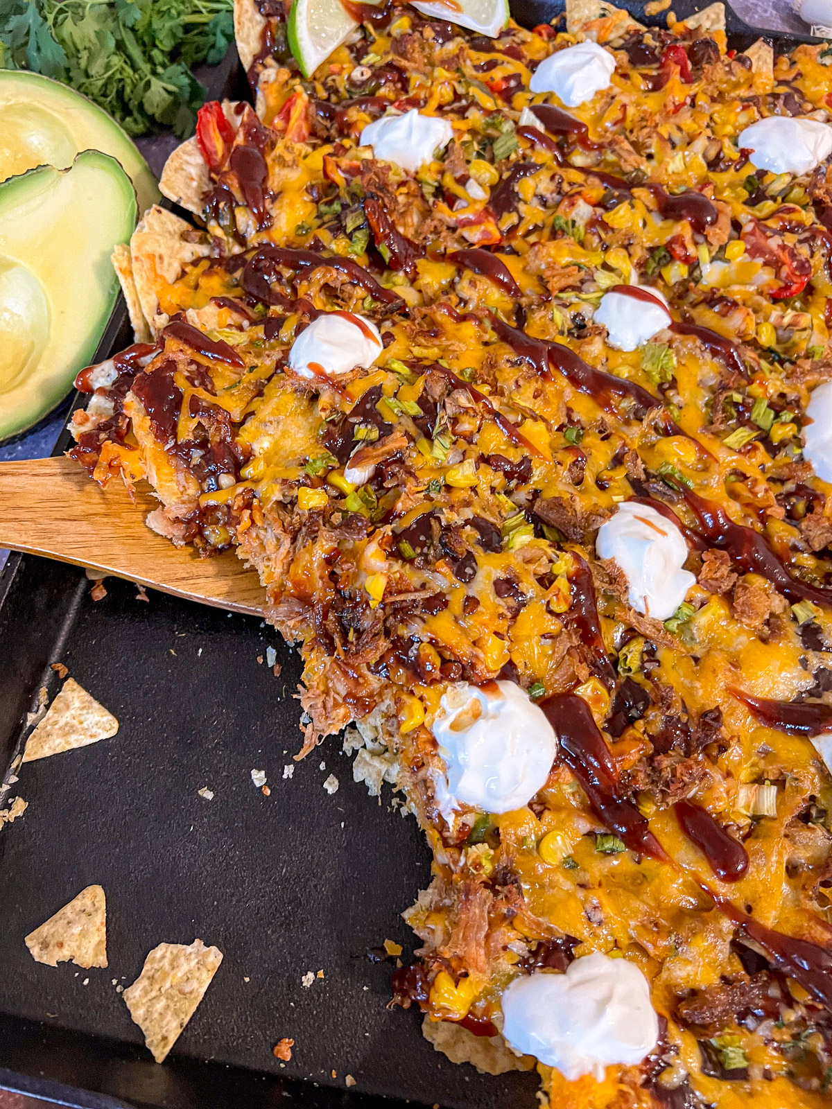 Wooden spatula pulling a section of pulled pork nachos showing cheese stretch and layers