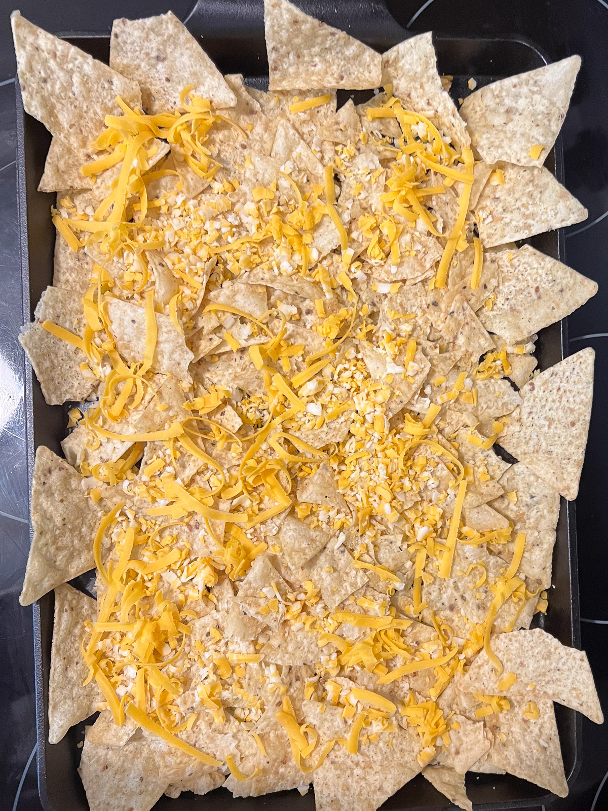 Shredded cheese sprinkled over the first layer of tortilla chips on a cast iron baking sheet
