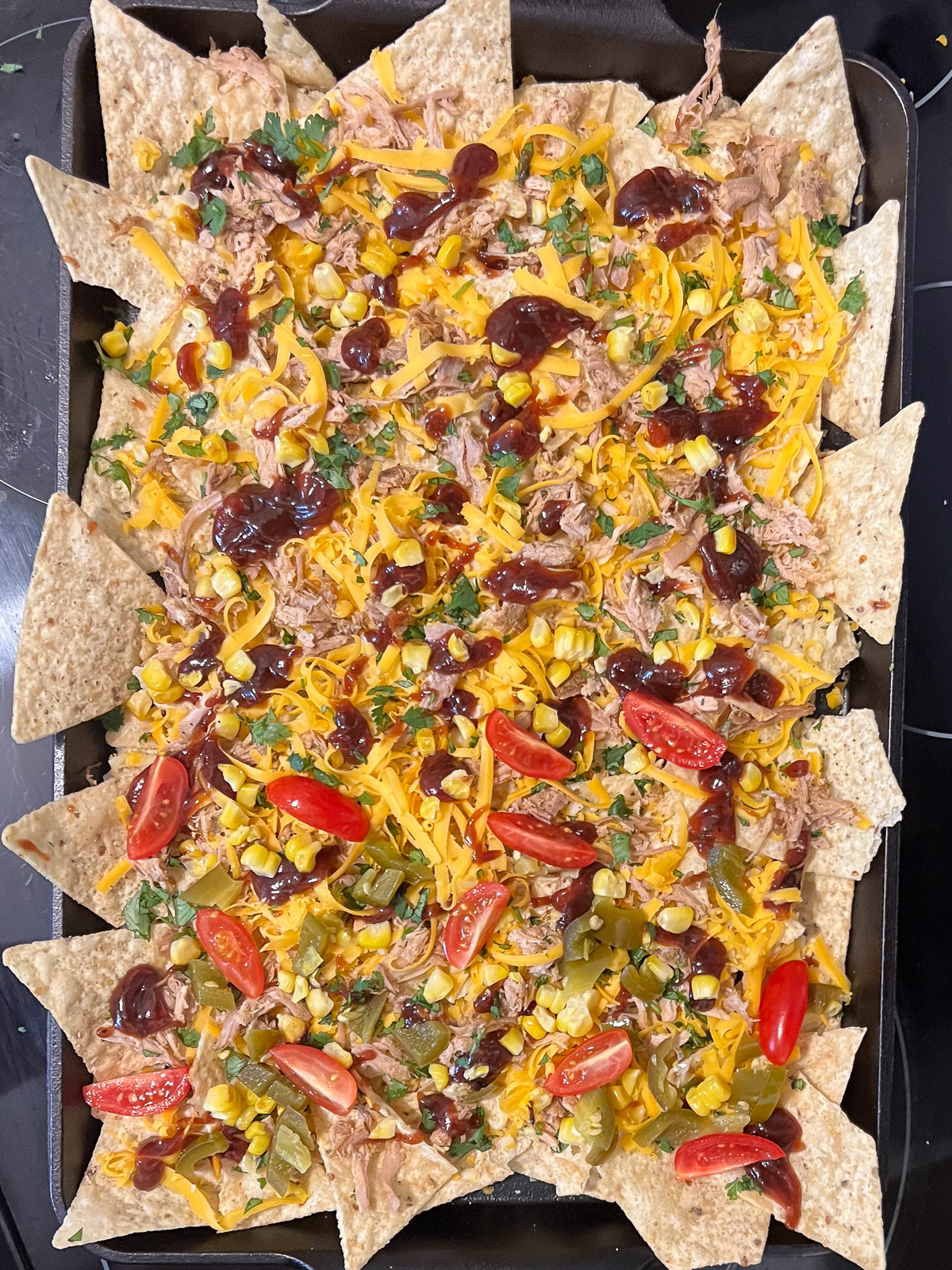 Pulled pork, roasted corn, and cilantro layered over chips and cheese on a cast iron baking sheet