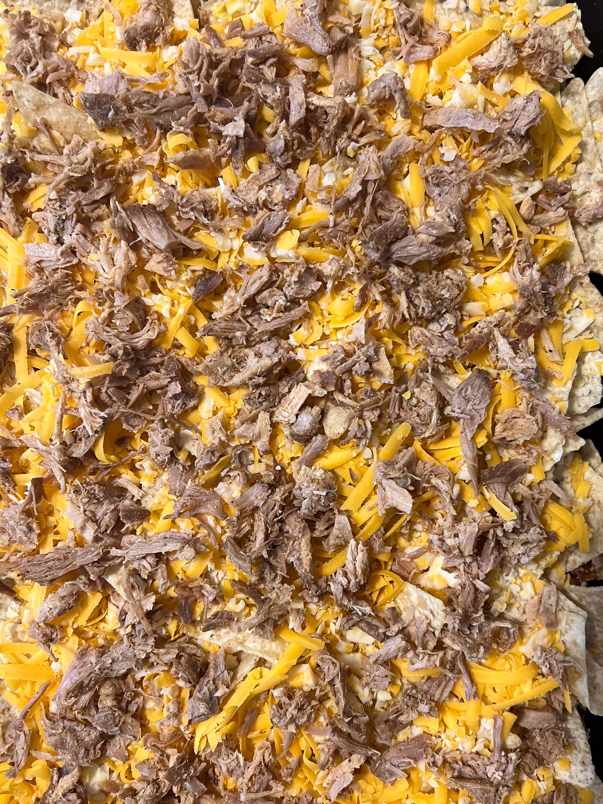 Building the second layer with cheese, pulled pork, corn, and toppings on the cast iron baking sheet