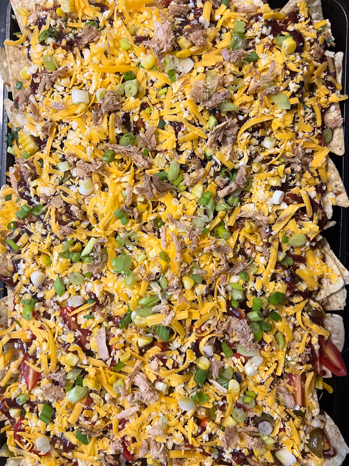 Fully assembled pulled pork nachos ready for the oven with green onions, cheese, and barbecue sauce