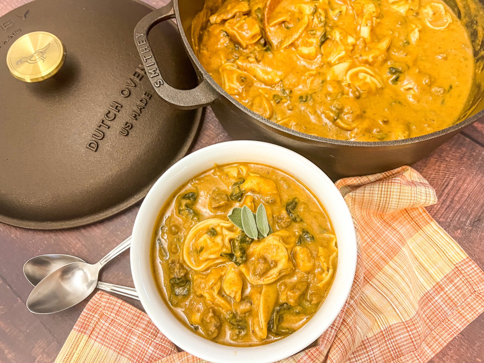 A hearty serving of butternut tortellini sausage soup in a white bowl with a rest in the dutch oven in the background.