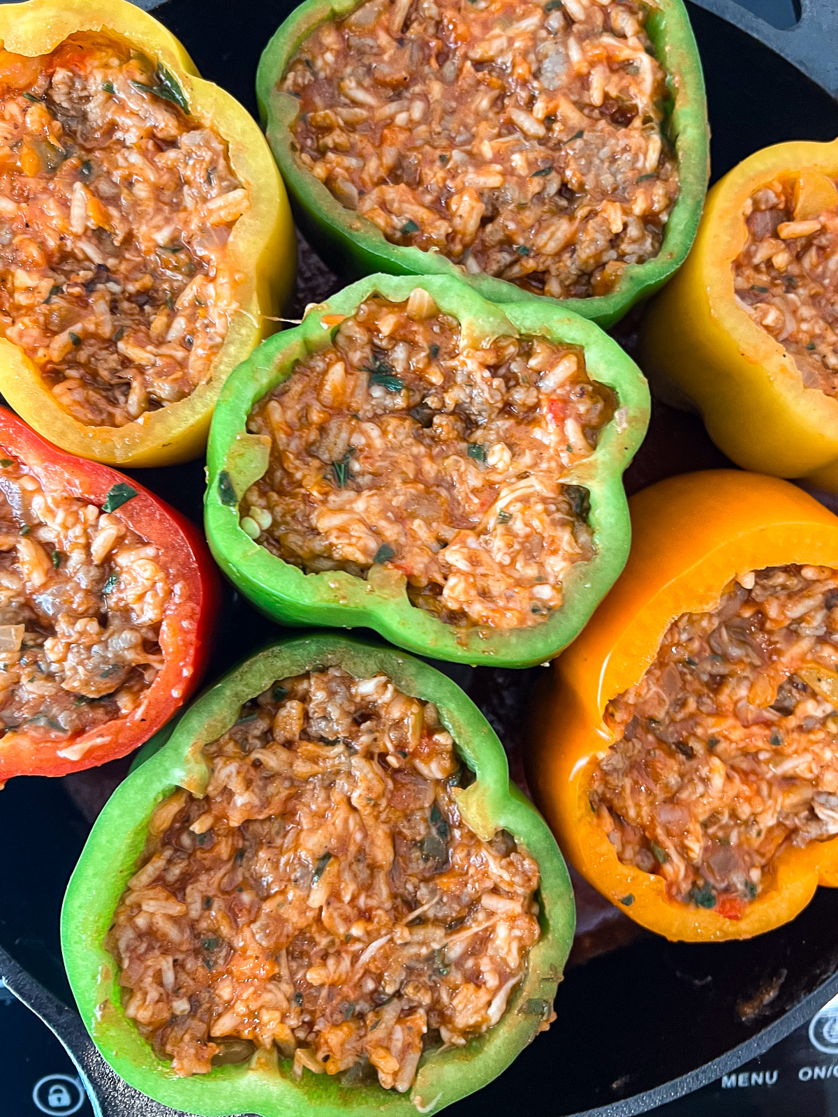 A bell pepper stuffed with the sausage and rice mixture placed in a cast iron skillet with sauce on the bottom.