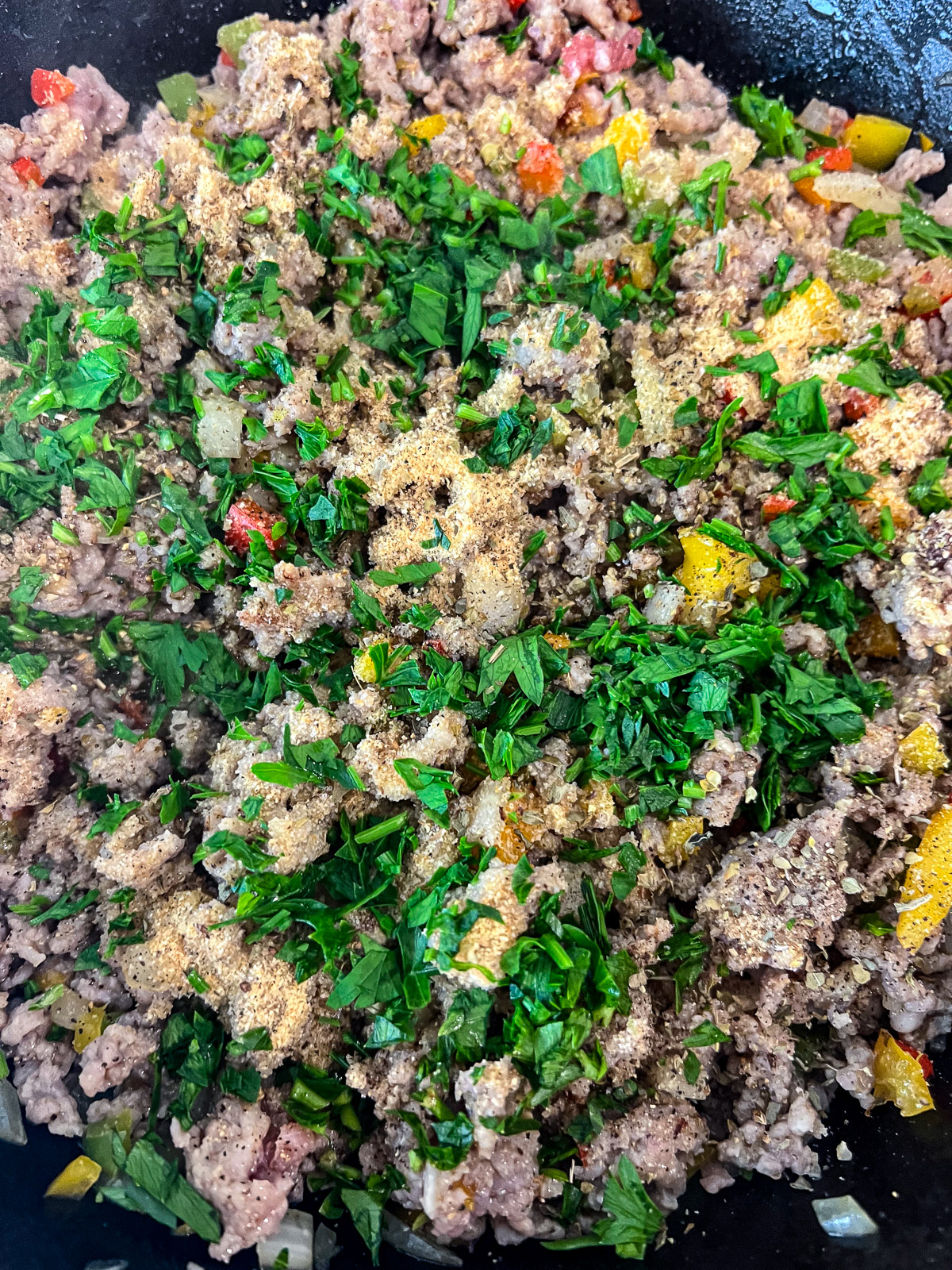 Italian sausage crumbled into a cast iron skillet with sautéed onions and peppers.