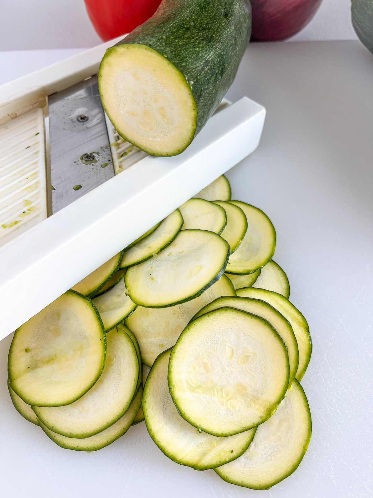 Zucchini being thinly sliced on a white mandolin slicer