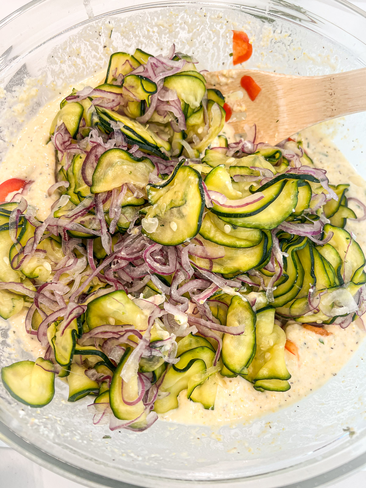 Drained zucchini and red onion being folded into the scarpaccia batter with a wooden spoon