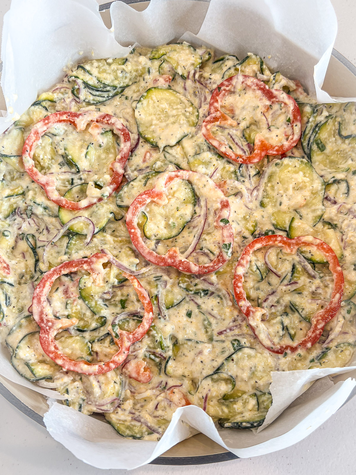 Unbaked scarpaccia pressed into a parchment-lined cast iron pan topped with decorative red bell pepper rings
