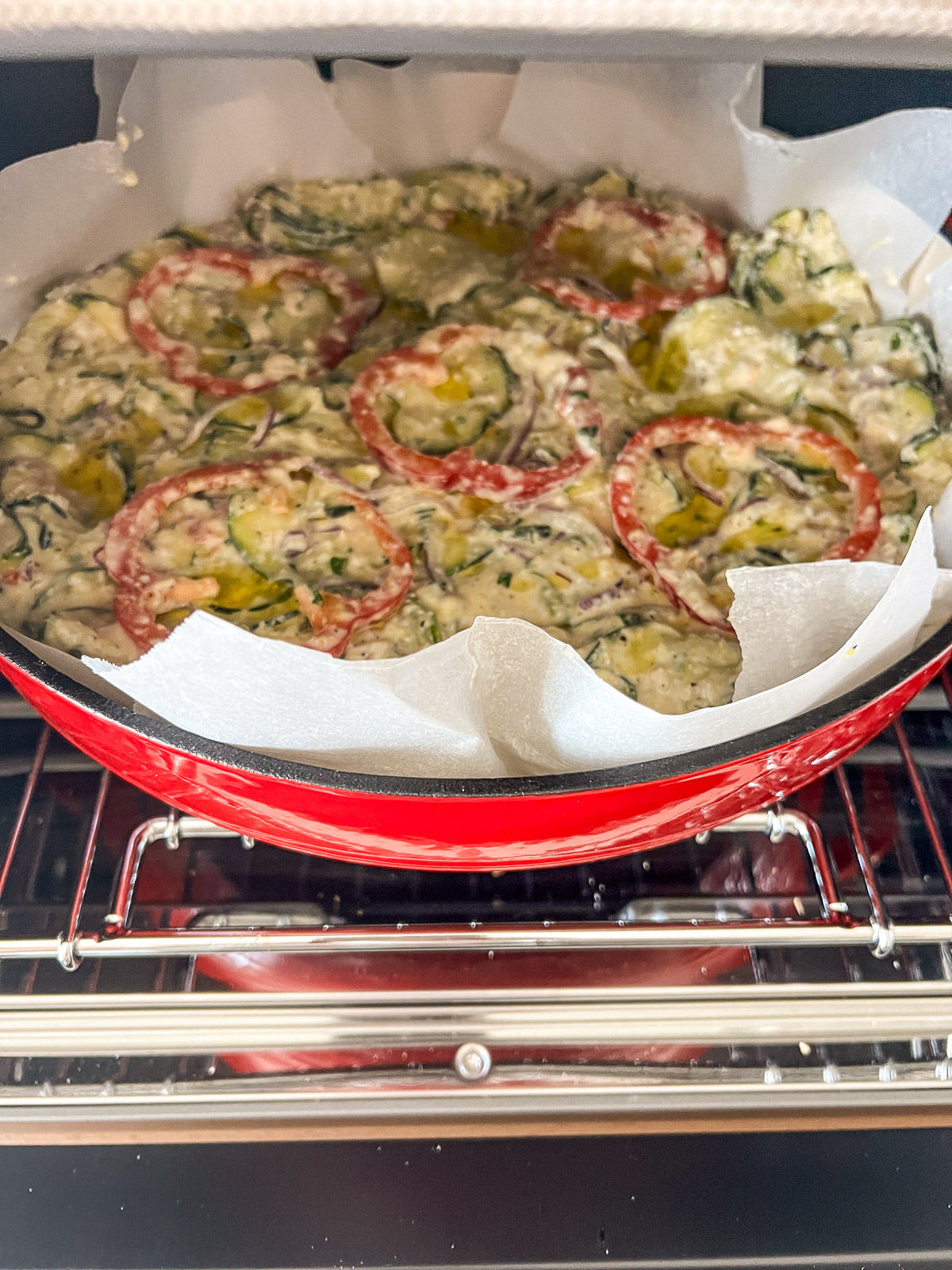 Unbaked scarpaccia in a red enameled cast iron Dutch oven going into the oven on a wire rack
