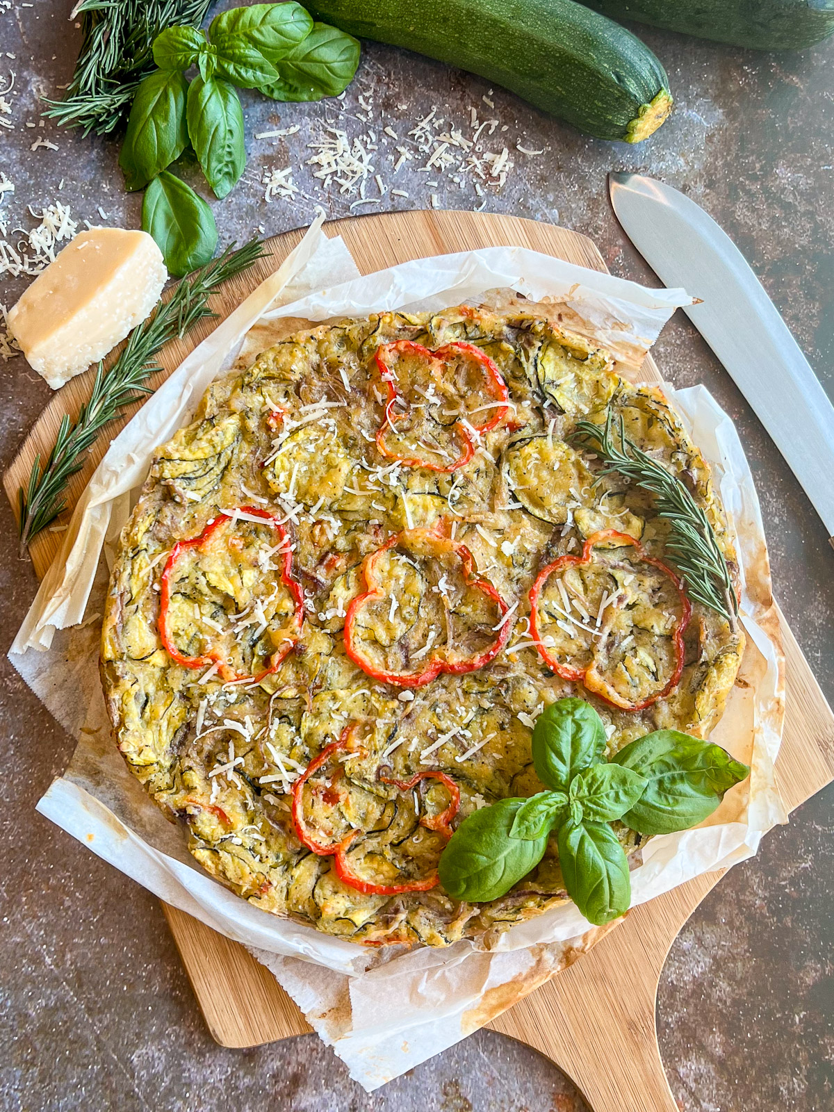 Scarpaccia Italian zucchini tart on a wooden cutting board garnished with fresh basil rosemary and shredded Parmesan cheese