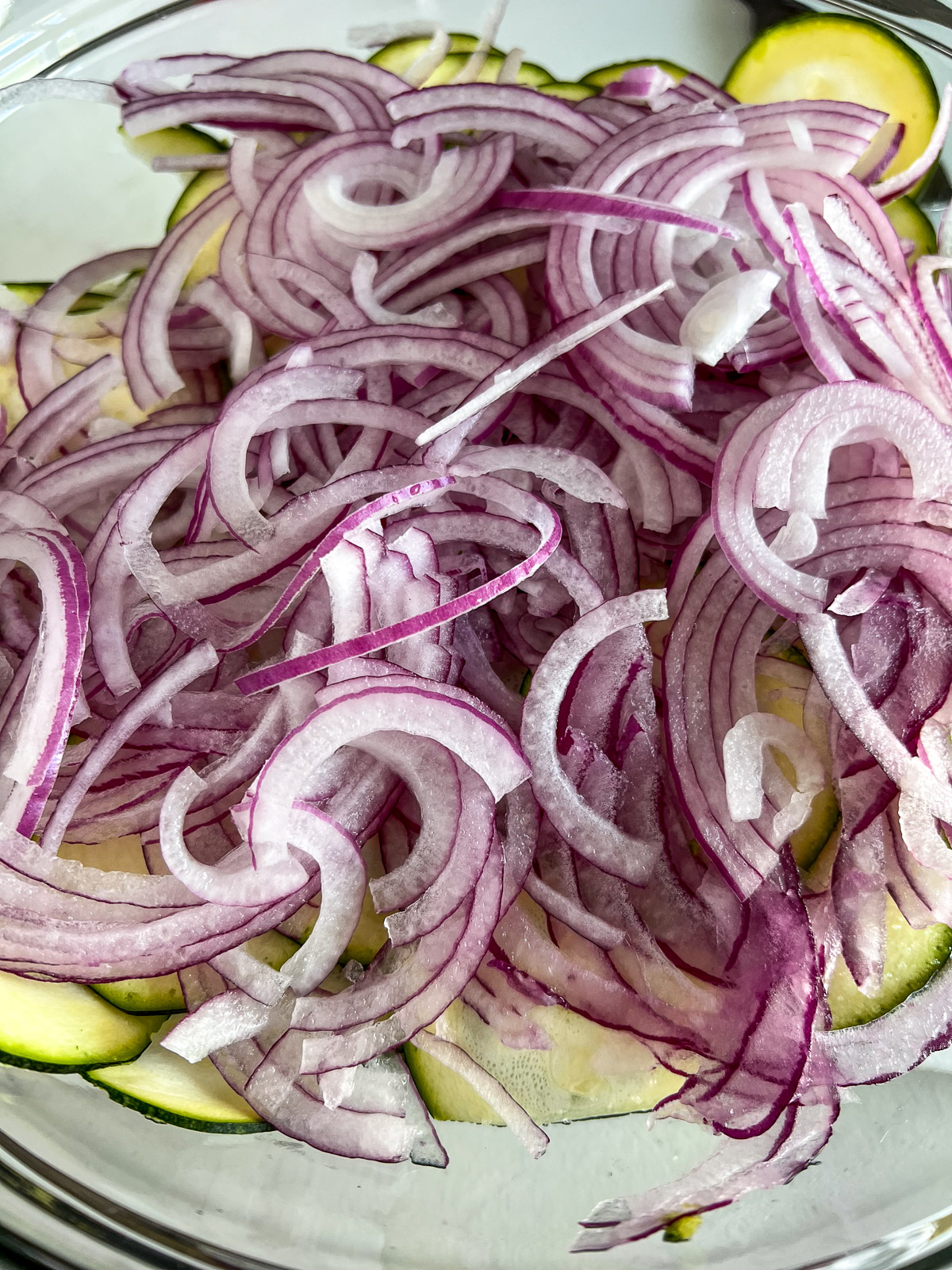 Thinly sliced red onion layered over mandolin-sliced zucchini in a glass bowl