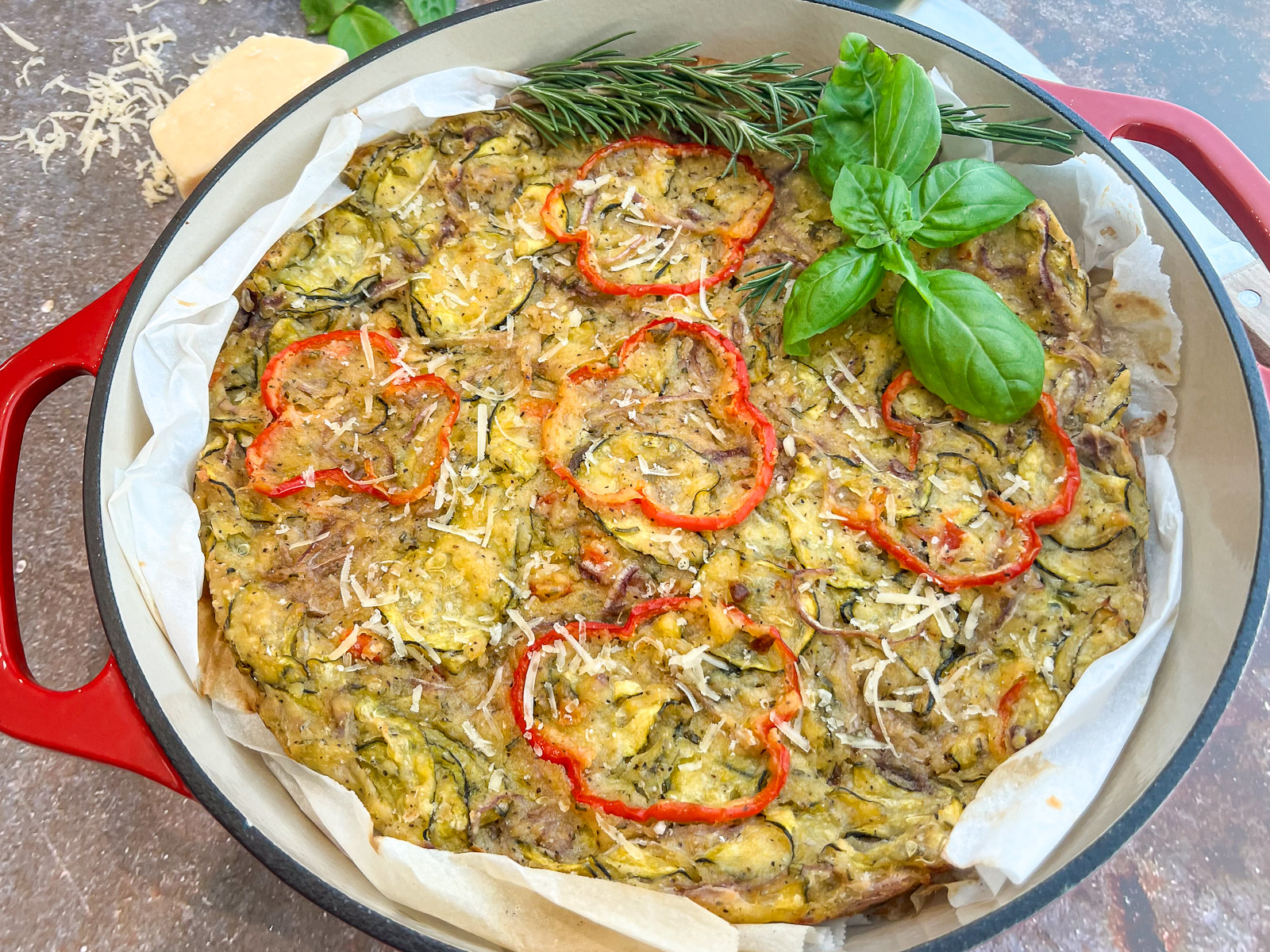 Freshly baked scarpaccia in a red enameled cast iron Dutch oven garnished with fresh basil rosemary and Parmesan