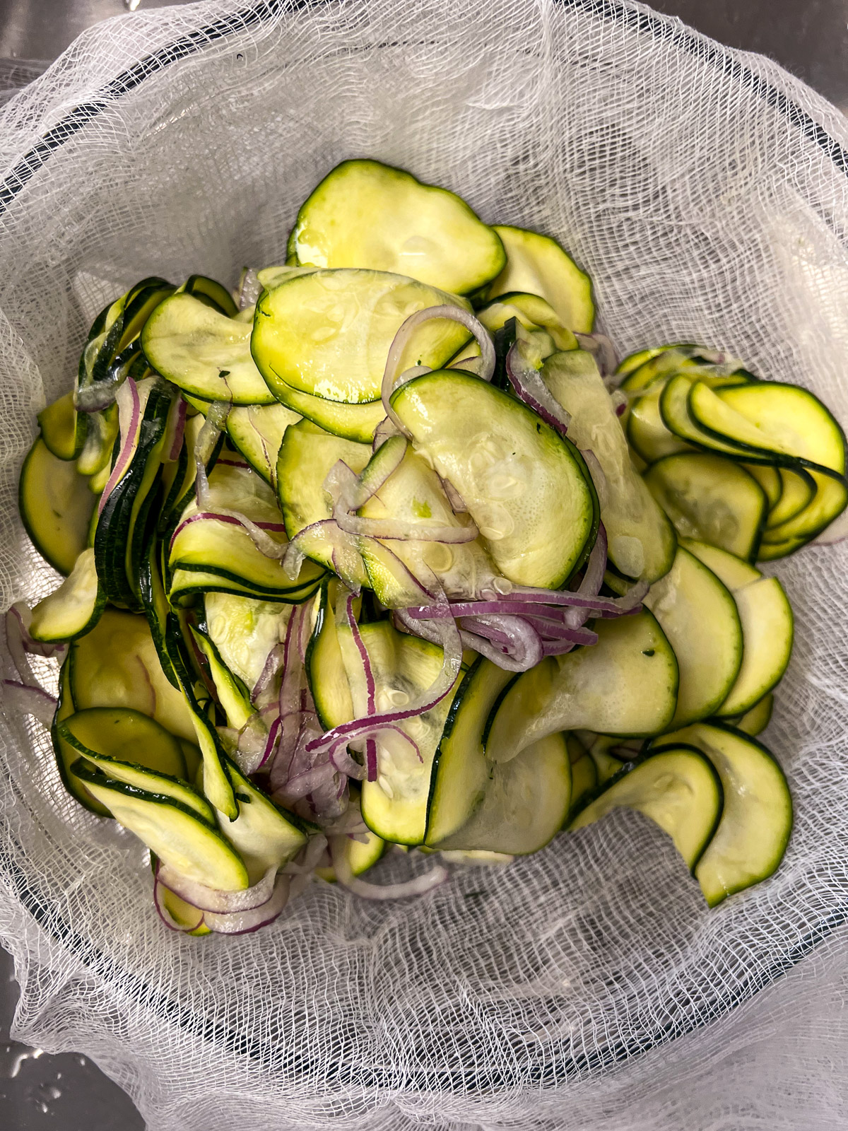 Drained zucchini and red onion wrapped in cheesecloth ready to squeeze out excess moisture