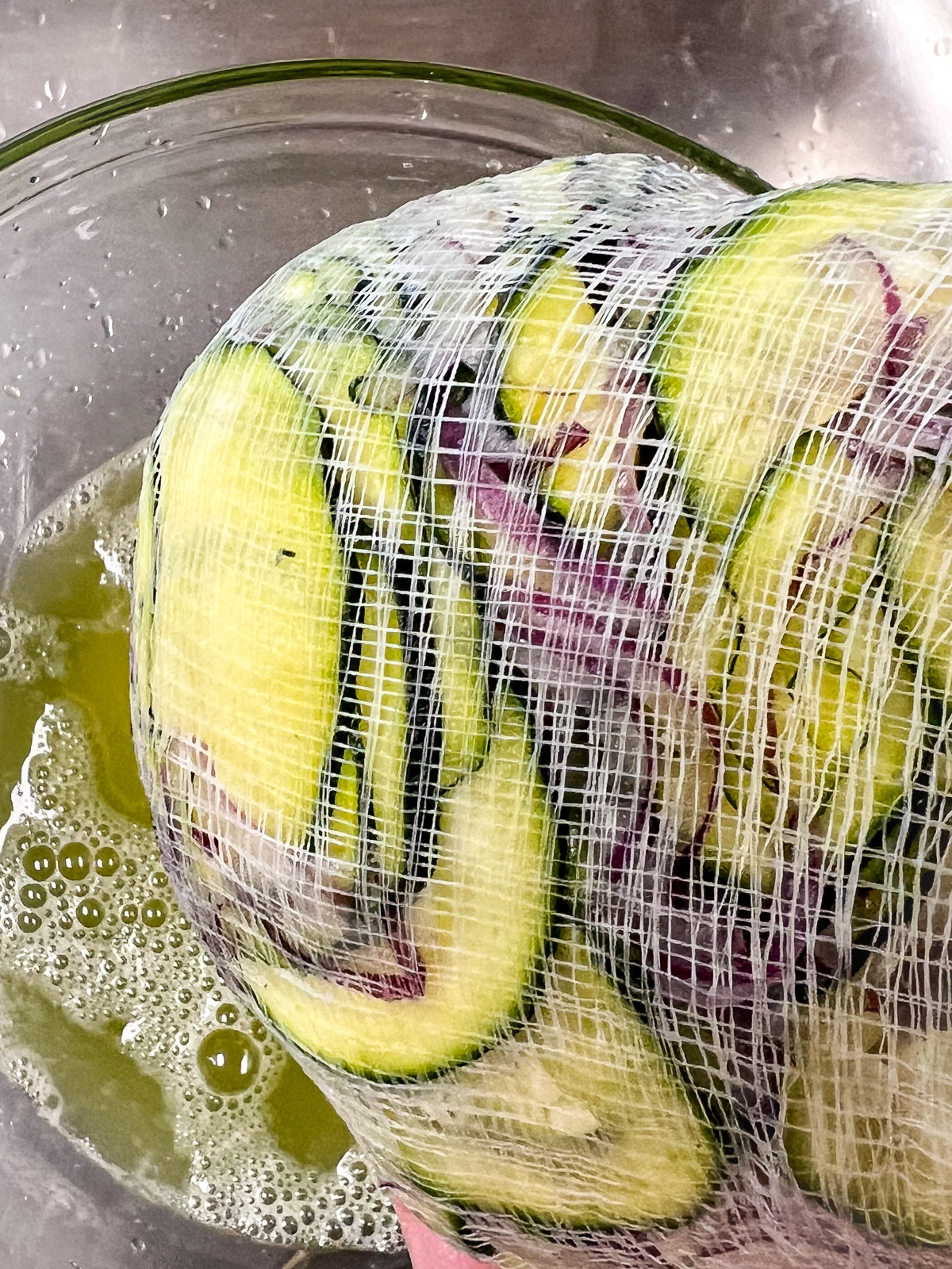 Squeezing moisture from zucchini through cheesecloth into a glass bowl