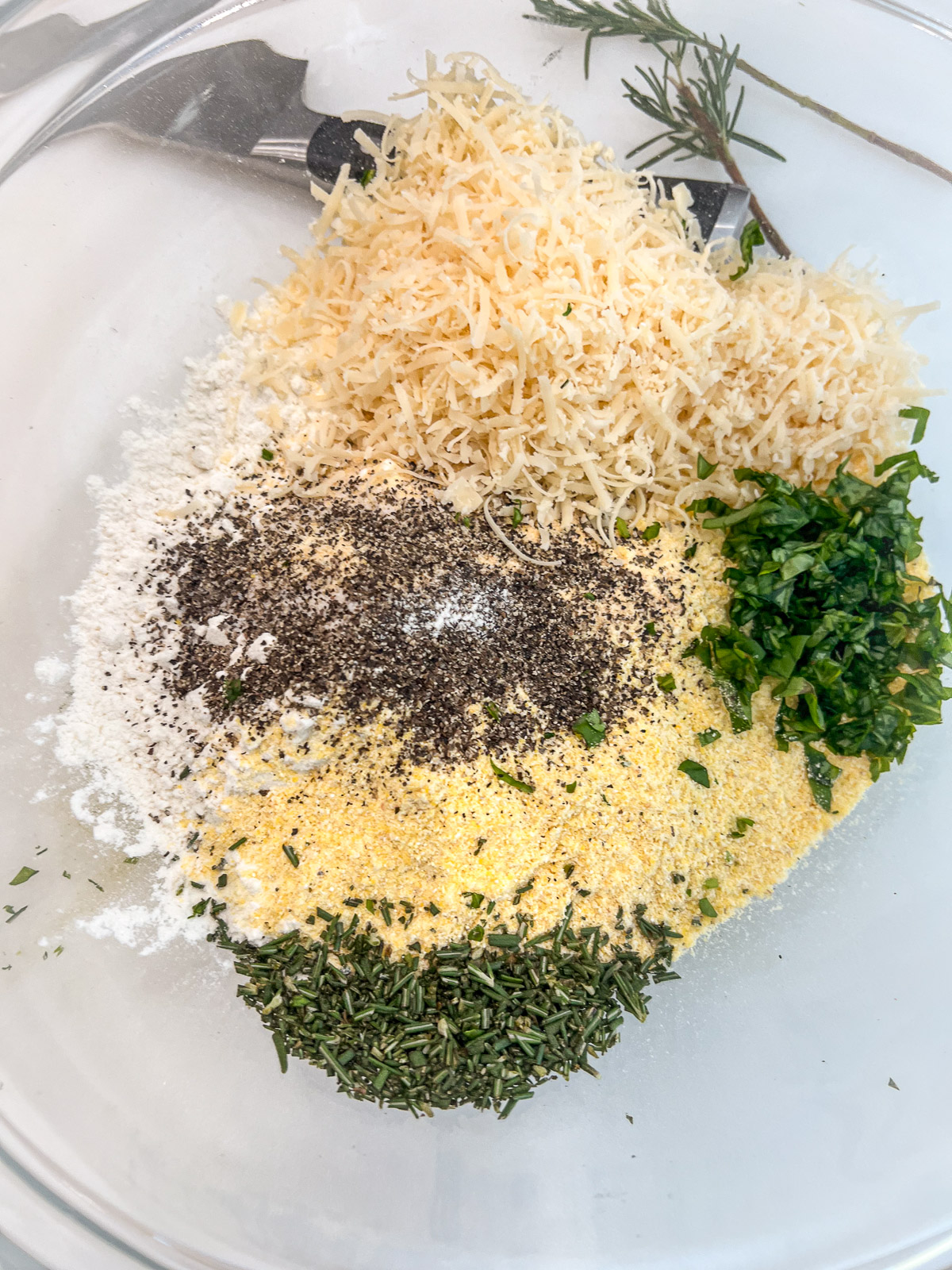 Dry ingredients for scarpaccia batter flour cornmeal shredded Parmesan chopped herbs and seasonings in a glass bowl