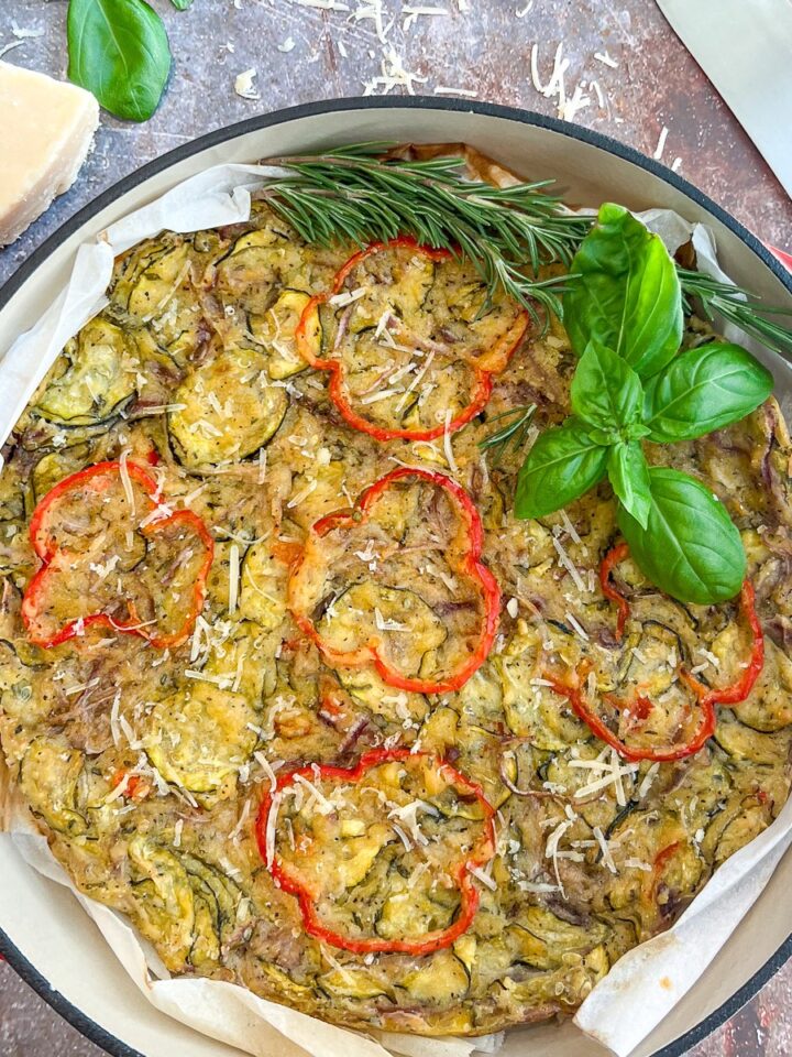 Scarpaccia Italian zucchini tart in a red enameled cast iron Dutch oven garnished with fresh basil and rosemary