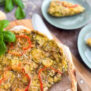 Sliced scarpaccia Italian zucchini tart on a wooden board with a serving on a green plate in the background