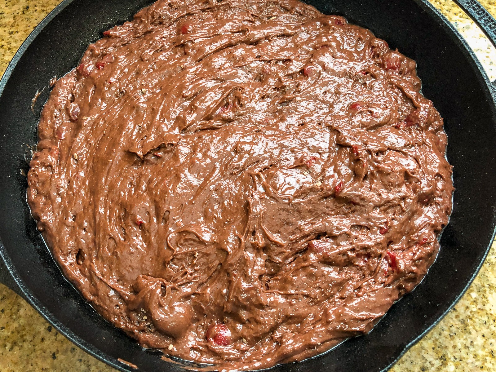 Cherry chocolate cake batter poured into a preheated cast iron skillet.
