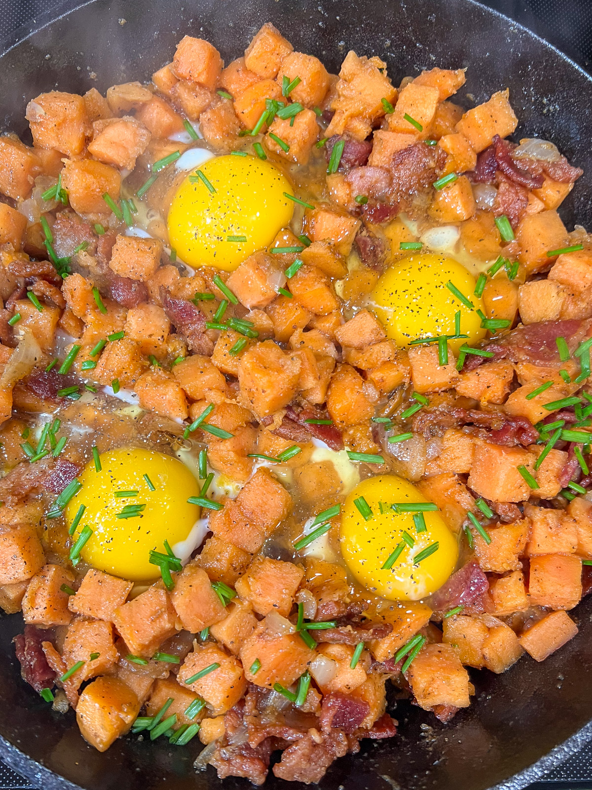 Eggs cracked into wells in the sweet potato hash in a cast iron skillet.