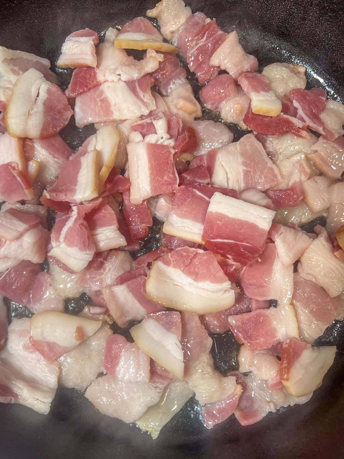 Crispy bacon cooking in a cast iron skillet for sweet potato hash.