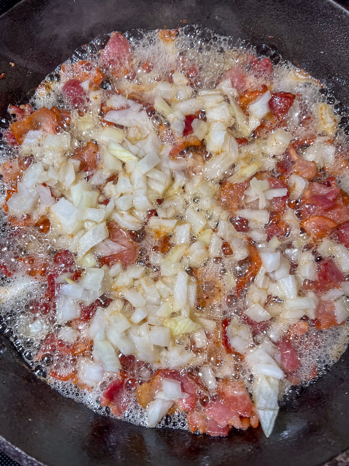 Diced onions sauteing in bacon fat in a cast iron skillet.