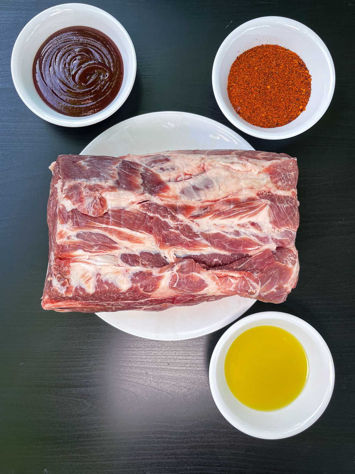 Ingredients for smoked pork butt: raw pork roast, BBQ sauce, dry rub, and olive oil.