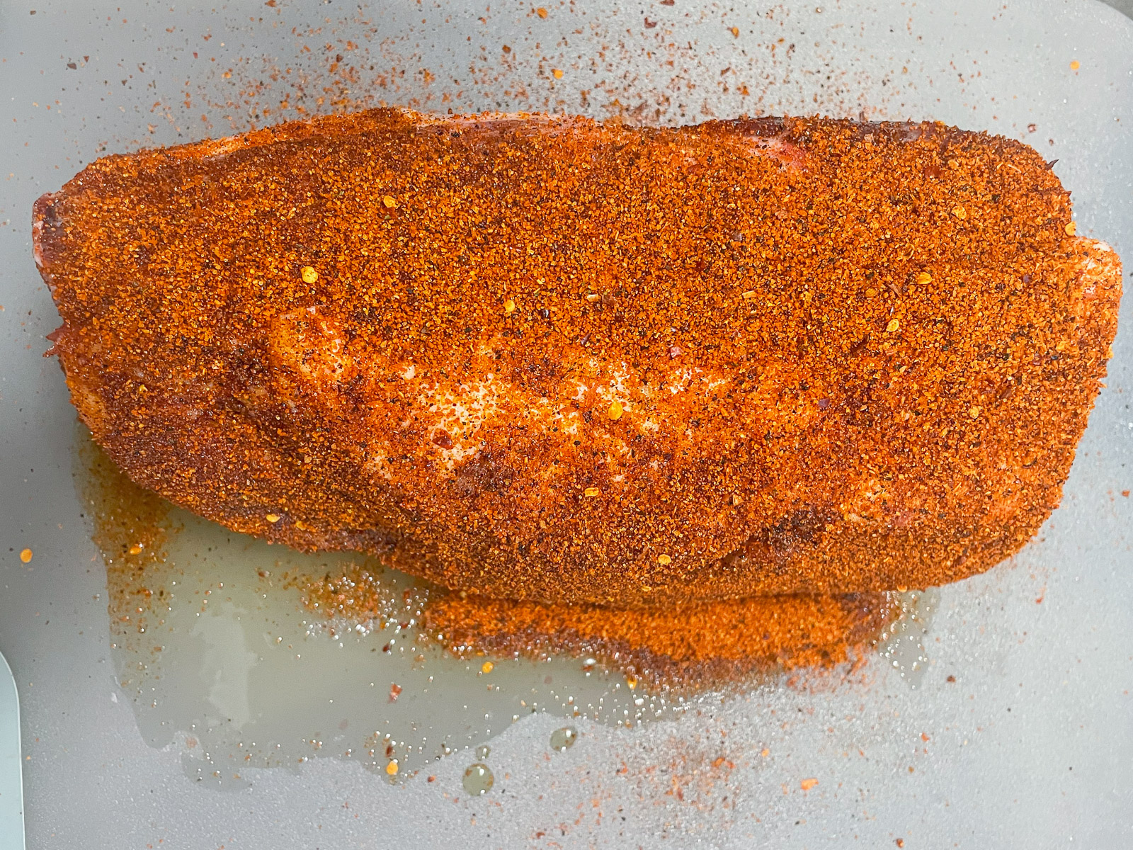 Pork butt coated in dry rub on a cutting board, ready for the smoker.