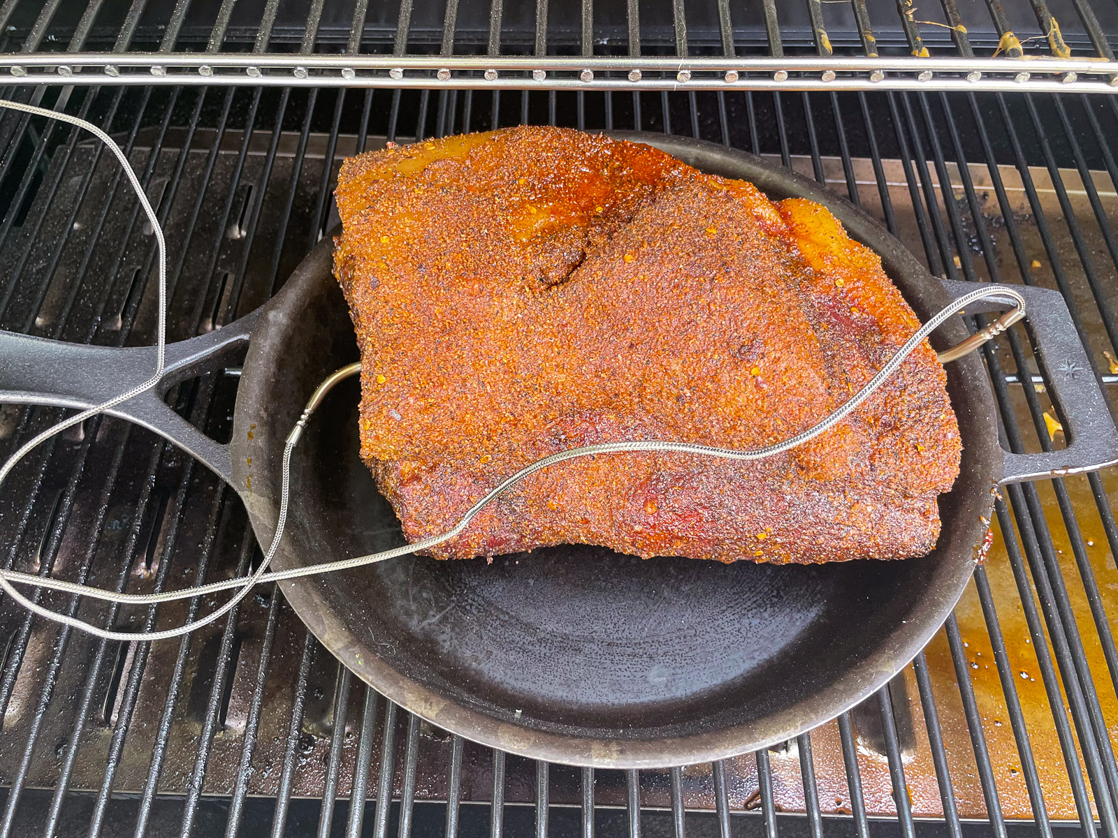 Smoked pork butt transferred to a cast iron skillet on the smoker grates.