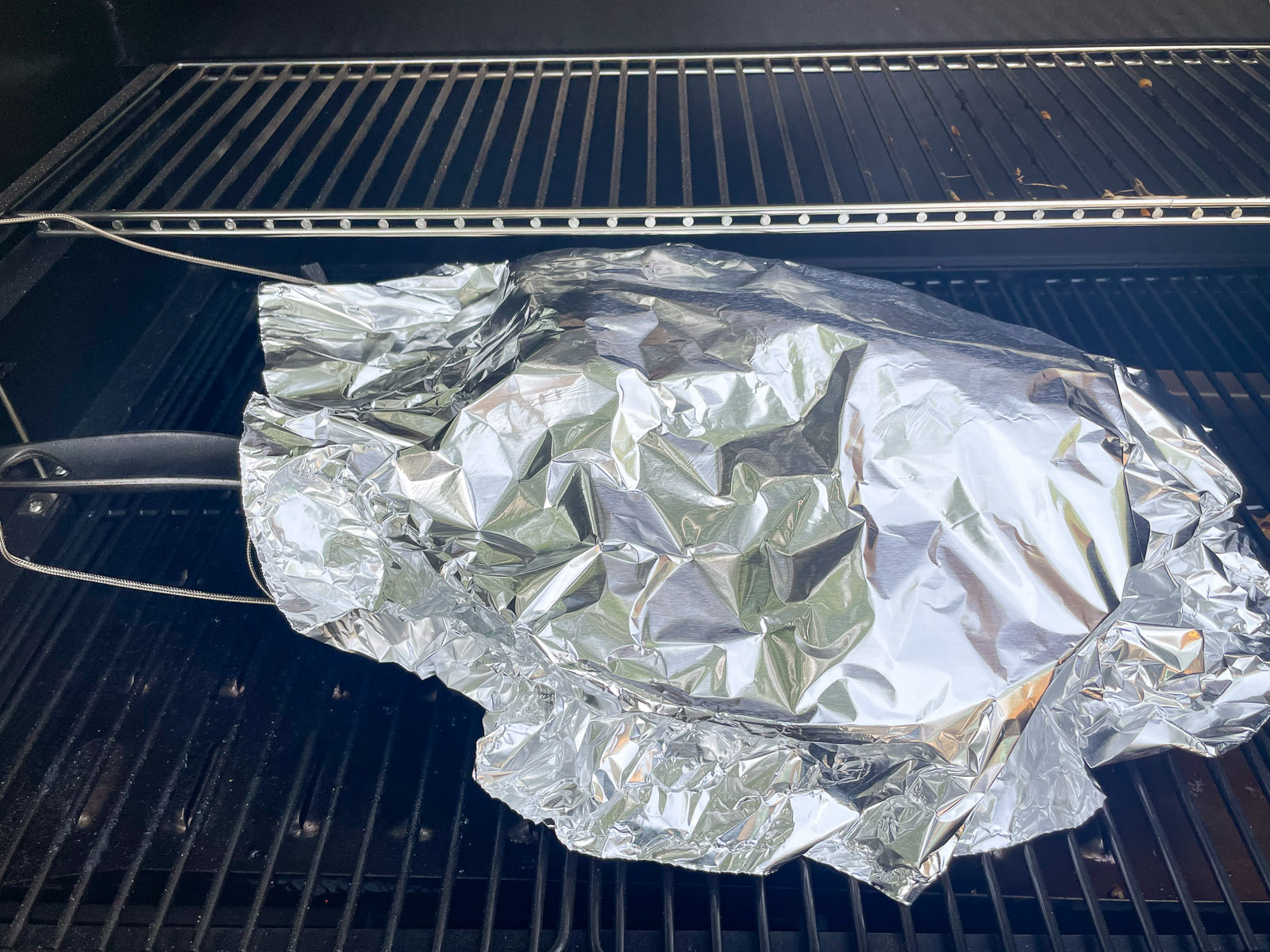 Pork butt wrapped in aluminum foil in a cast iron skillet on the smoker.