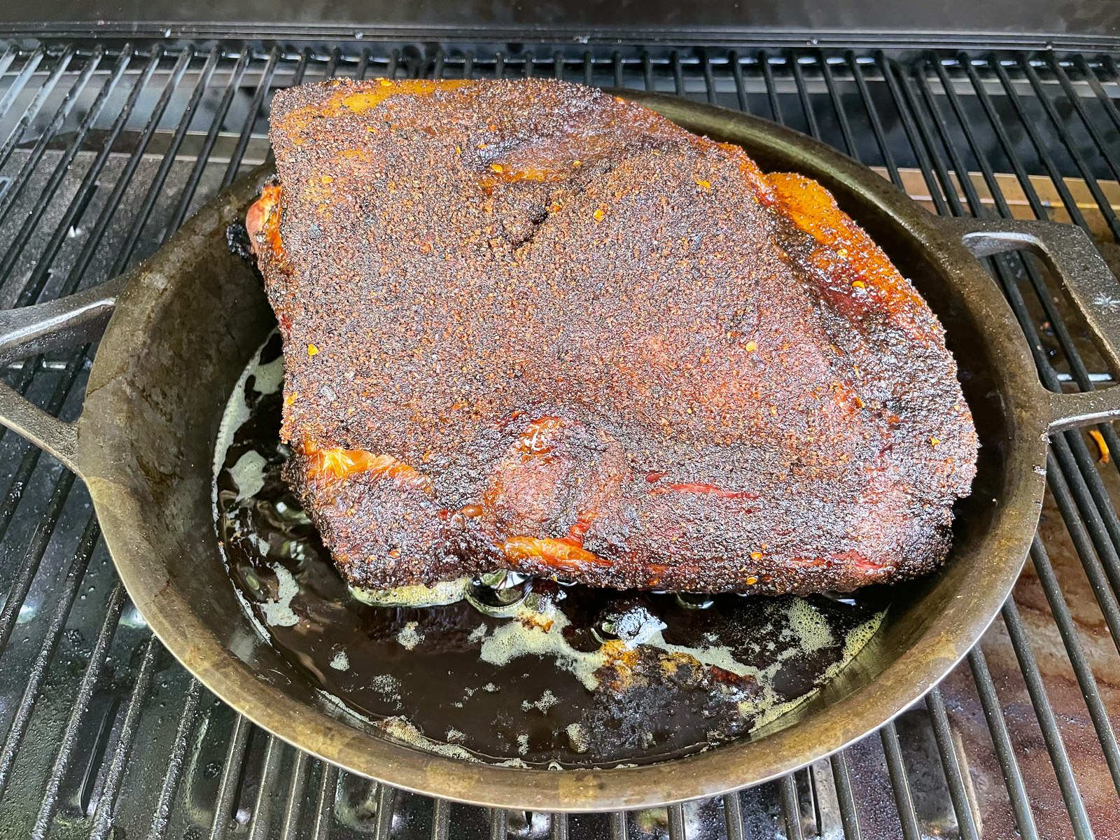 Smoked pork butt with deep mahogany bark in a cast iron skillet with rendered juices.