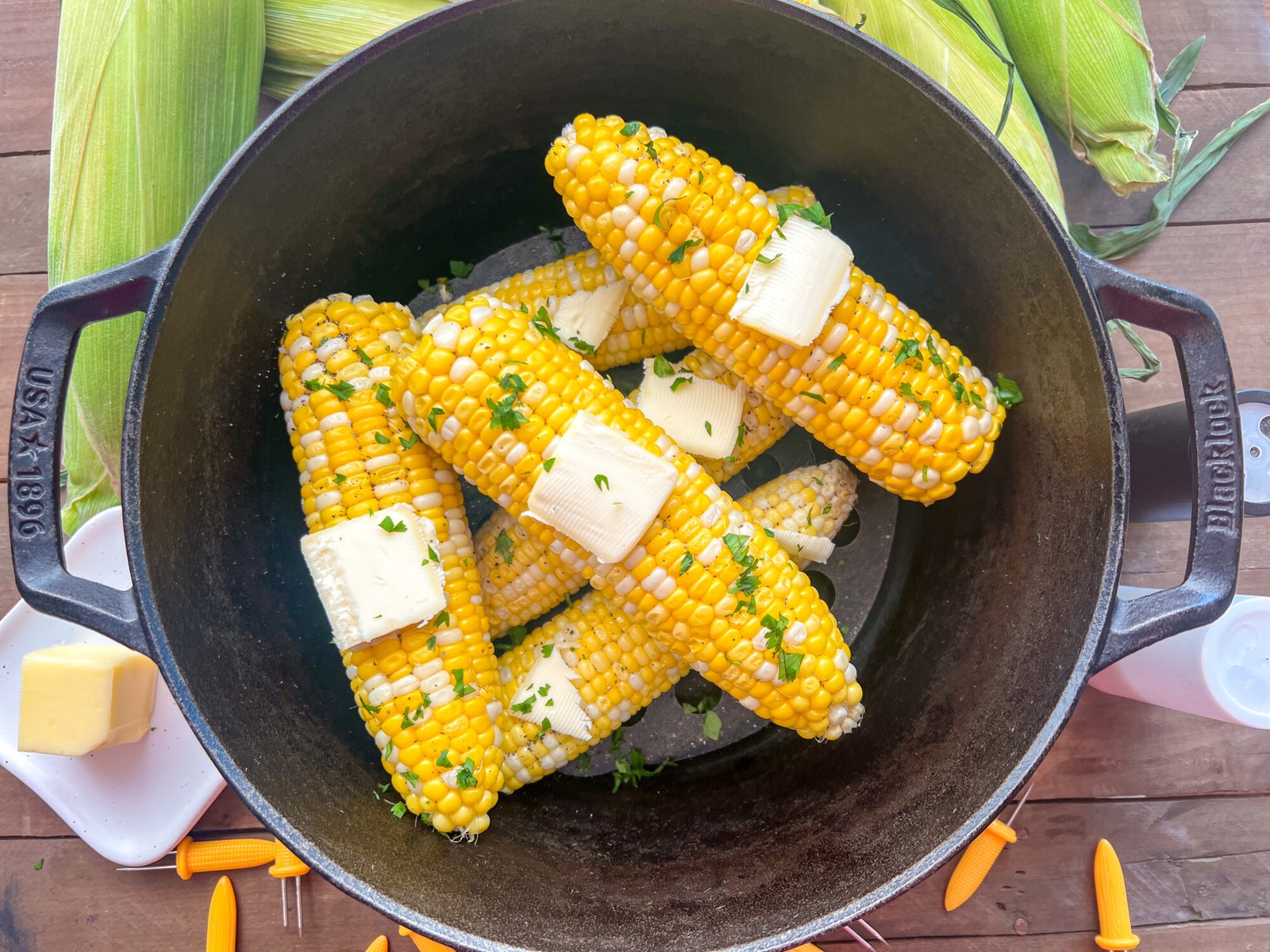 Freshly steamed corn on the cob in a dutch oven with butter and chopped parsley.