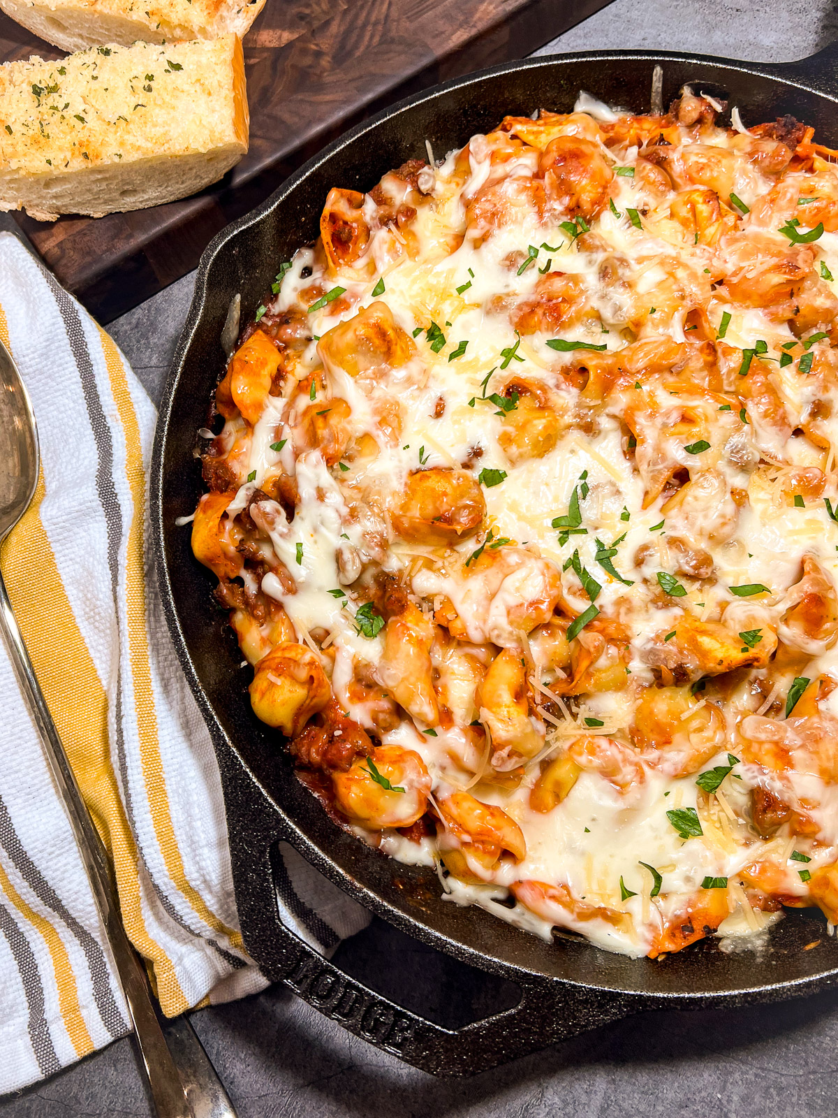 Overhead view of baked tortellini with sausage in cast iron skillet with garlic bread