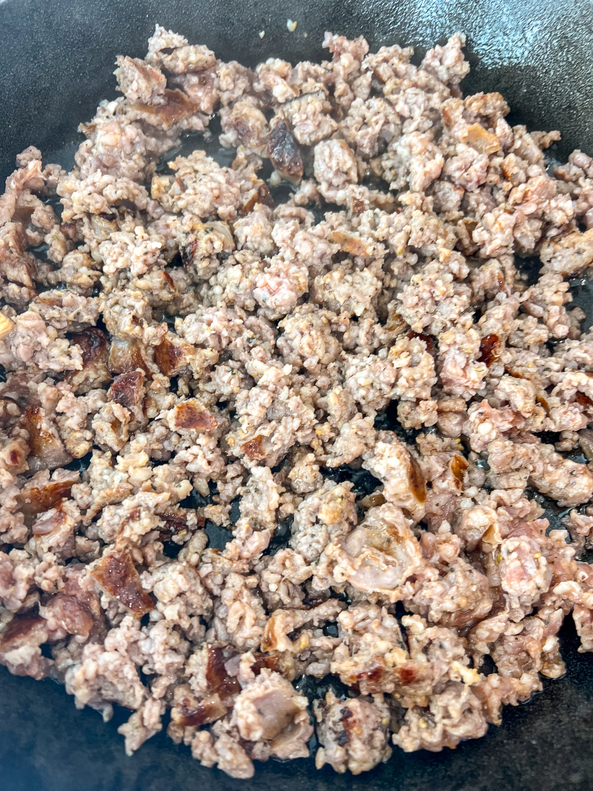 Browned Italian sausage crumbled in a cast iron skillet