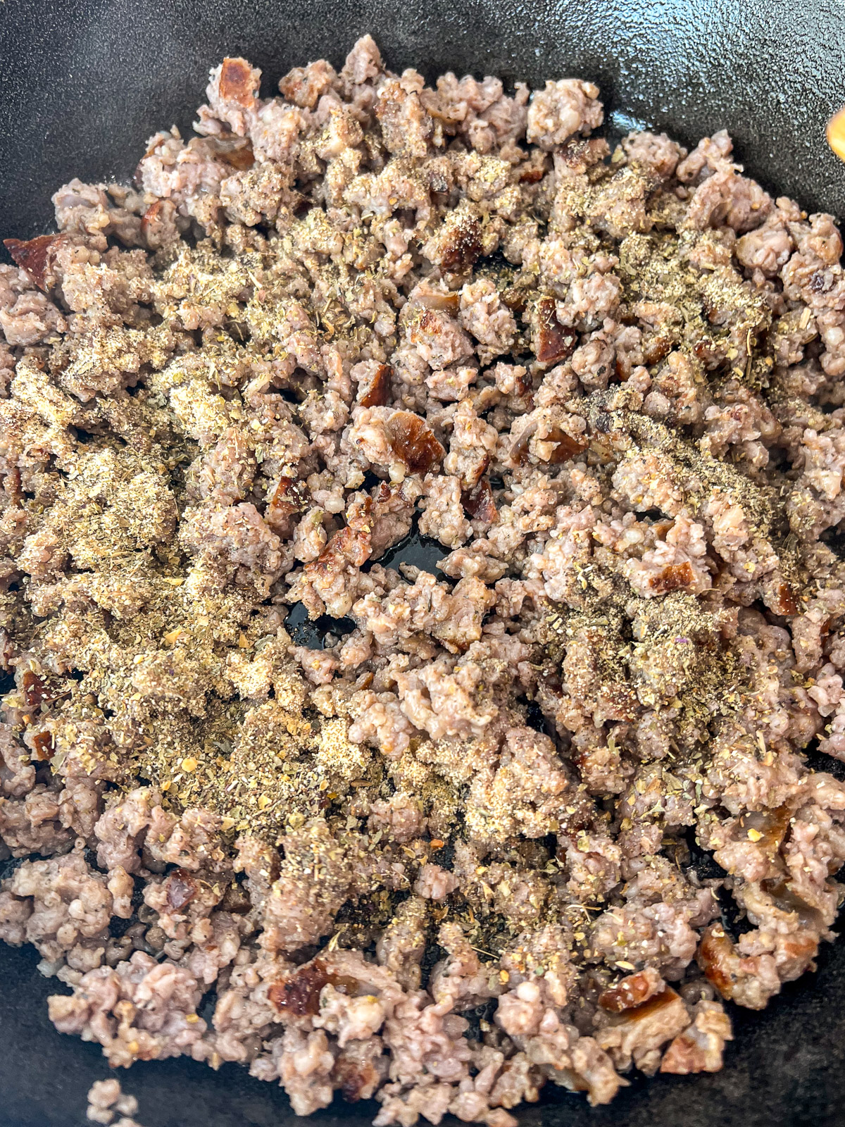 Browned Italian sausage with oregano and garlic seasonings in cast iron skillet
