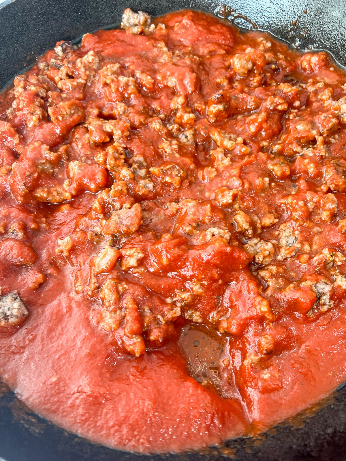 Marinara sauce added to Italian sausage in cast iron skillet