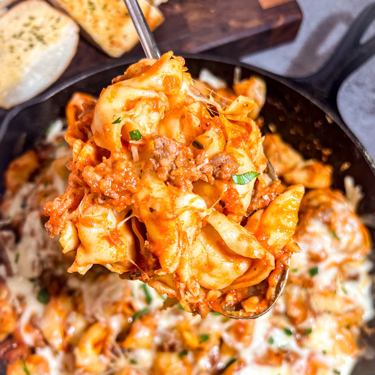 Spoon scooping tortellini with sausage from cast iron skillet