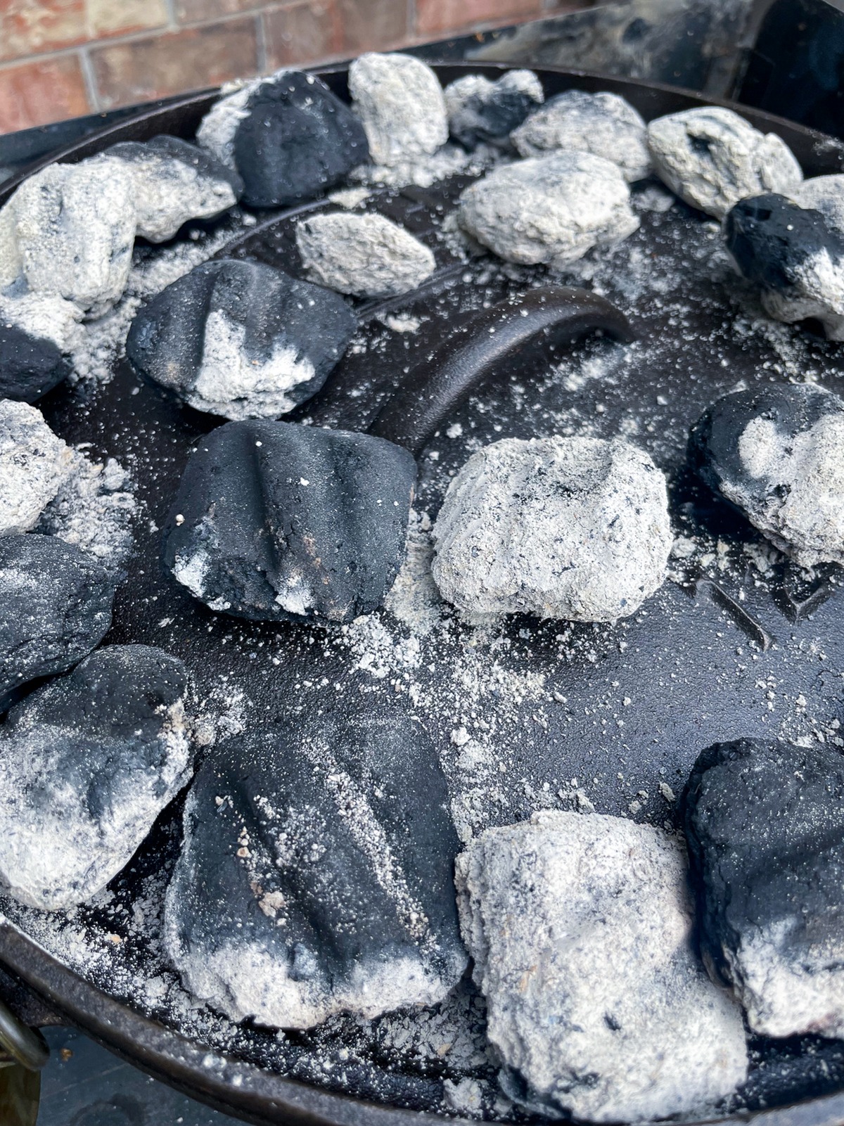 Close-up of white-gray ash coals on a Dutch oven lid - the optimal coal color for steady, even heat