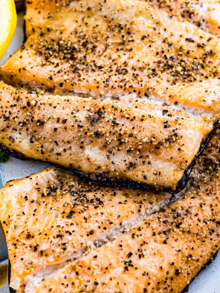 Grilled rainbow trout fillets in a cast iron skillet with lemon slices