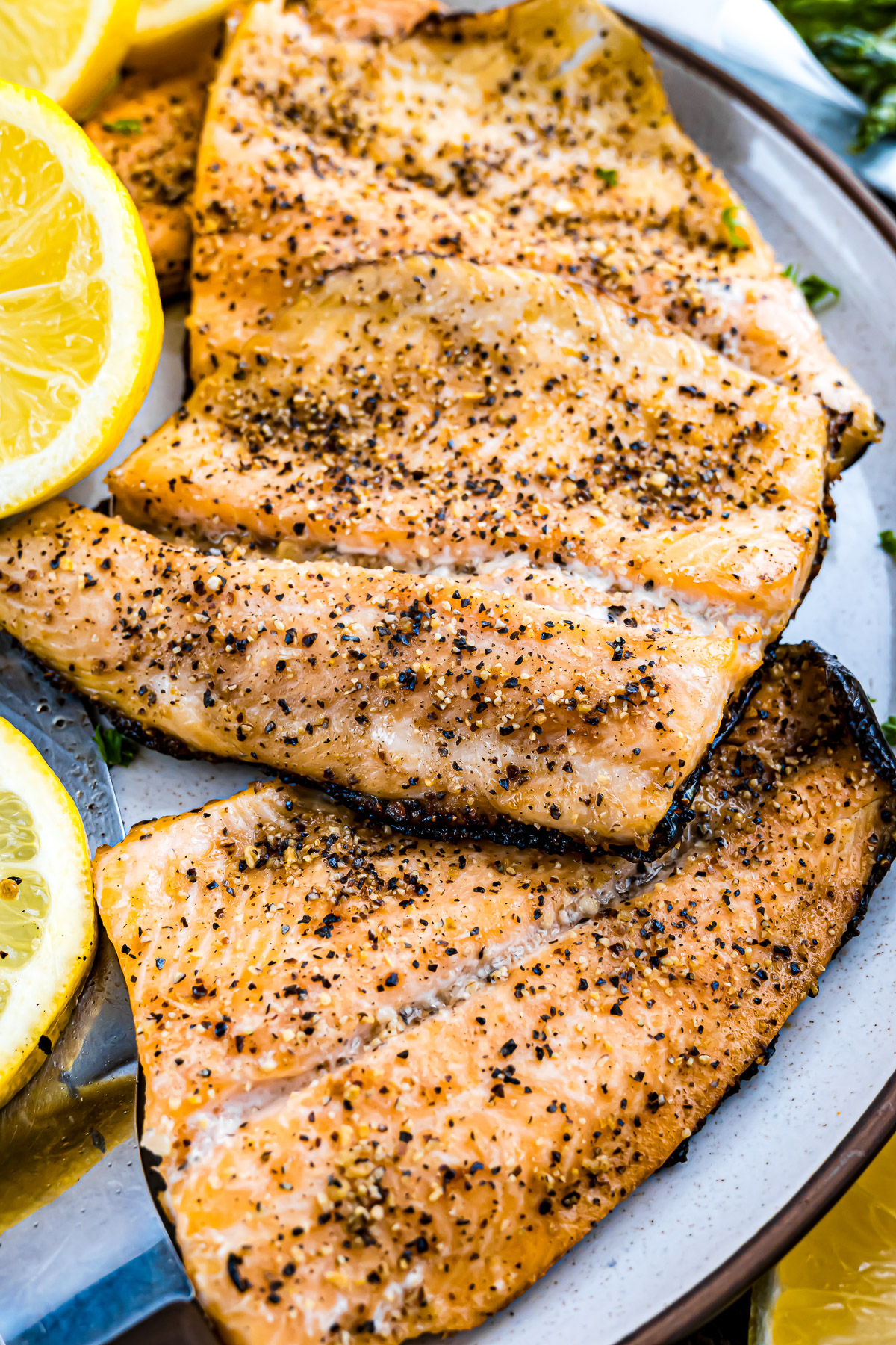 Grilled rainbow trout fillets with lemon pepper seasoning served on a plate with fresh lemon slices