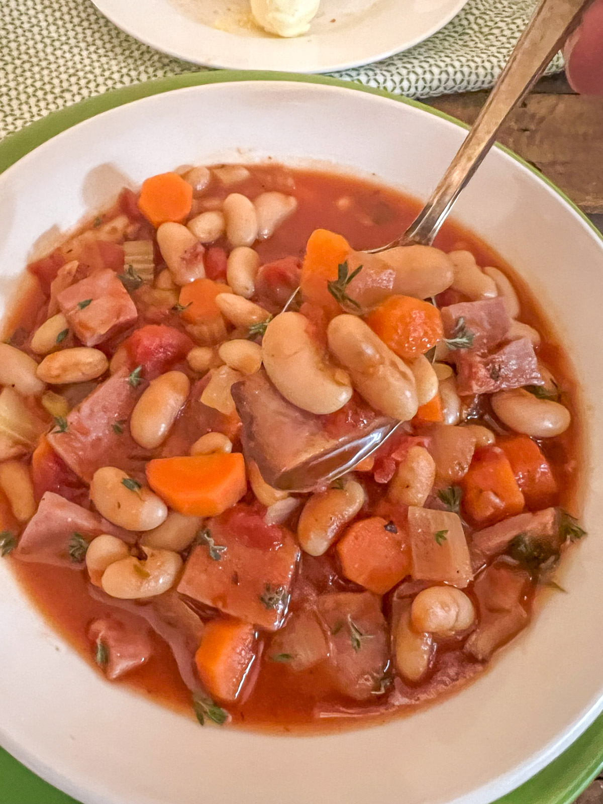 Bowl of ham and bean soup with tomatoes topped with fresh herbs