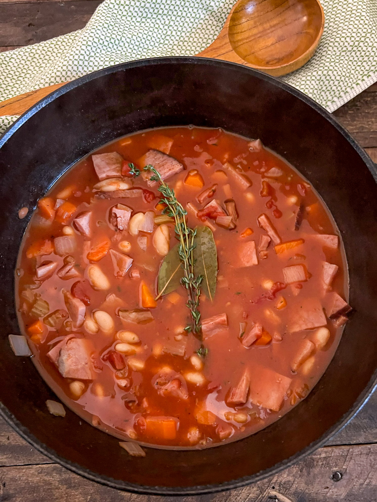 Ham and bean soup with tomatoes served from a Dutch oven with a wooden ladle